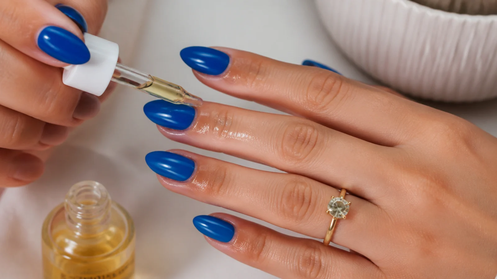 Cuticle oil being massaged around finished glossy royal blue nails