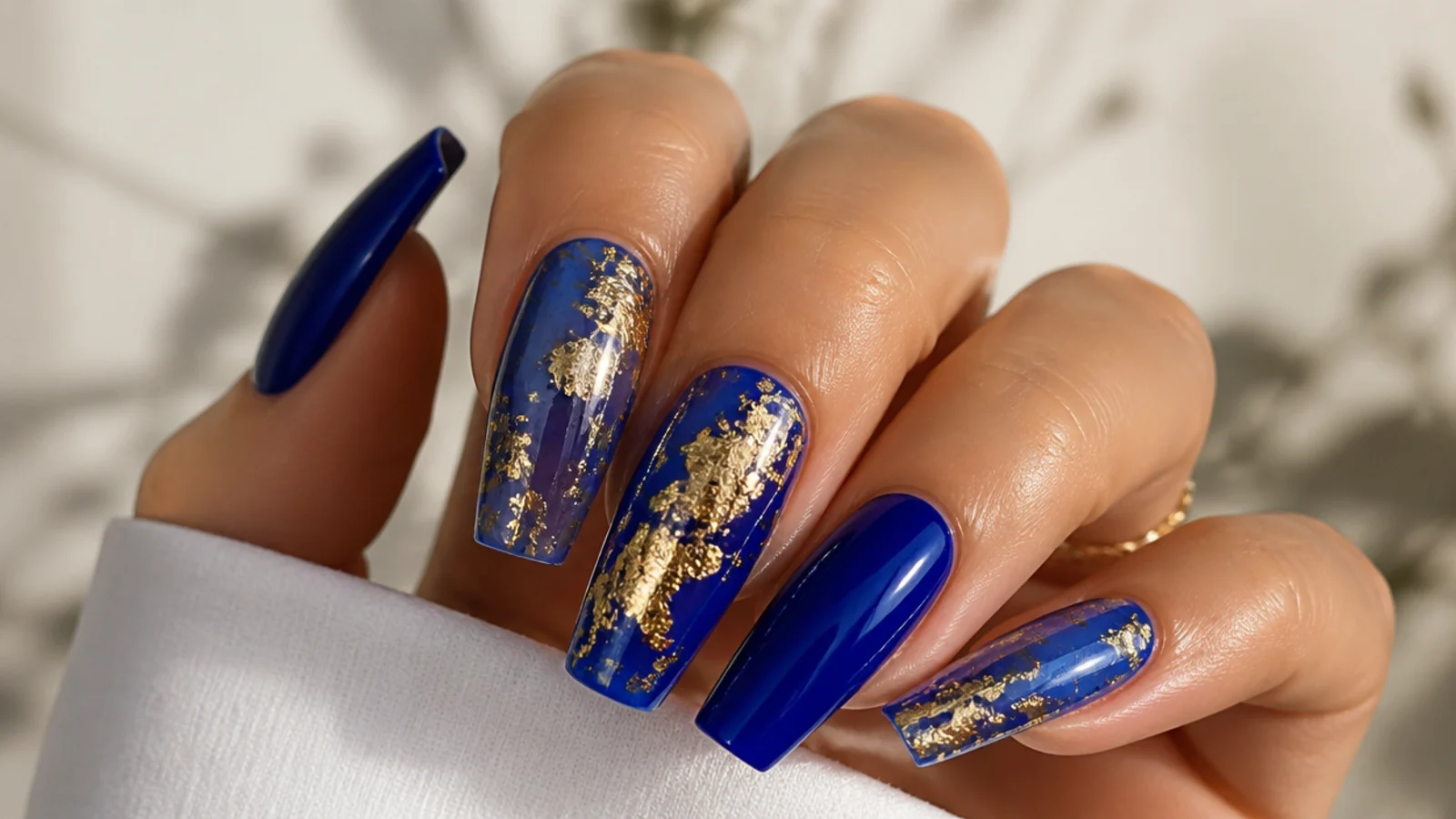 Royal blue acrylic nails with gold foil accents in a coffin shape