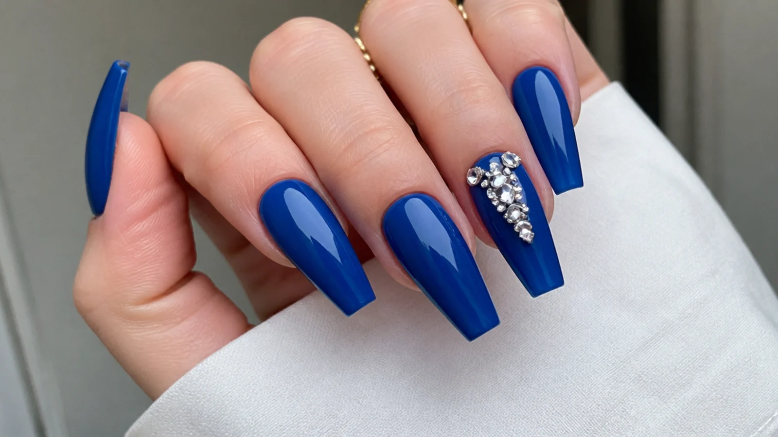 Royal blue acrylic nails with clustered clear rhinestones on one accent nail