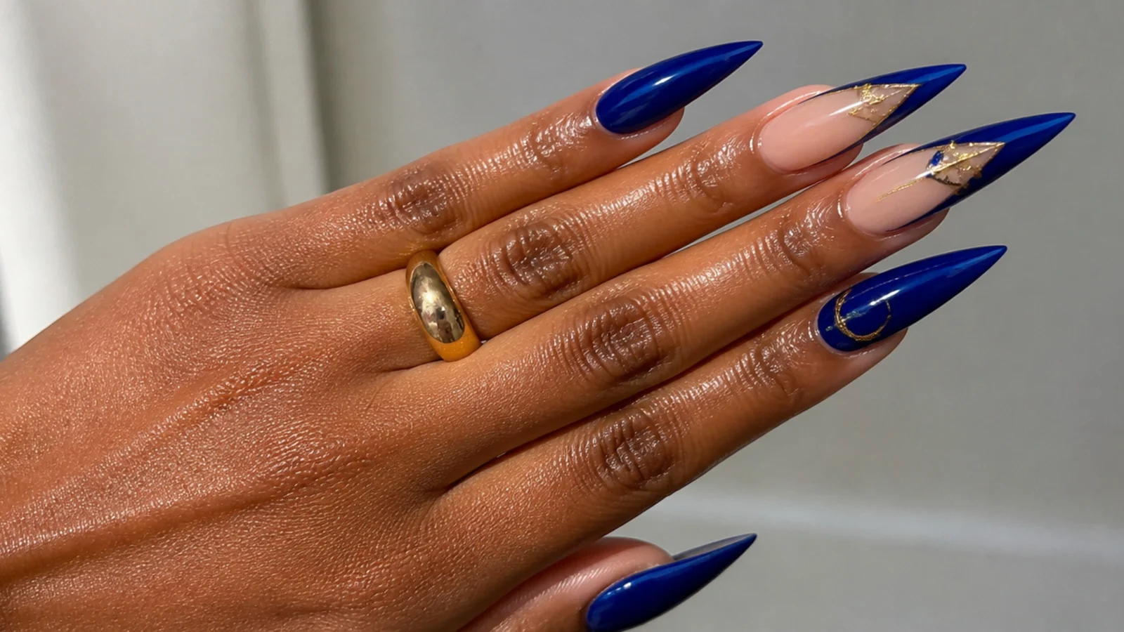 Long royal blue acrylic nails in a sharp stiletto shape on deep skin