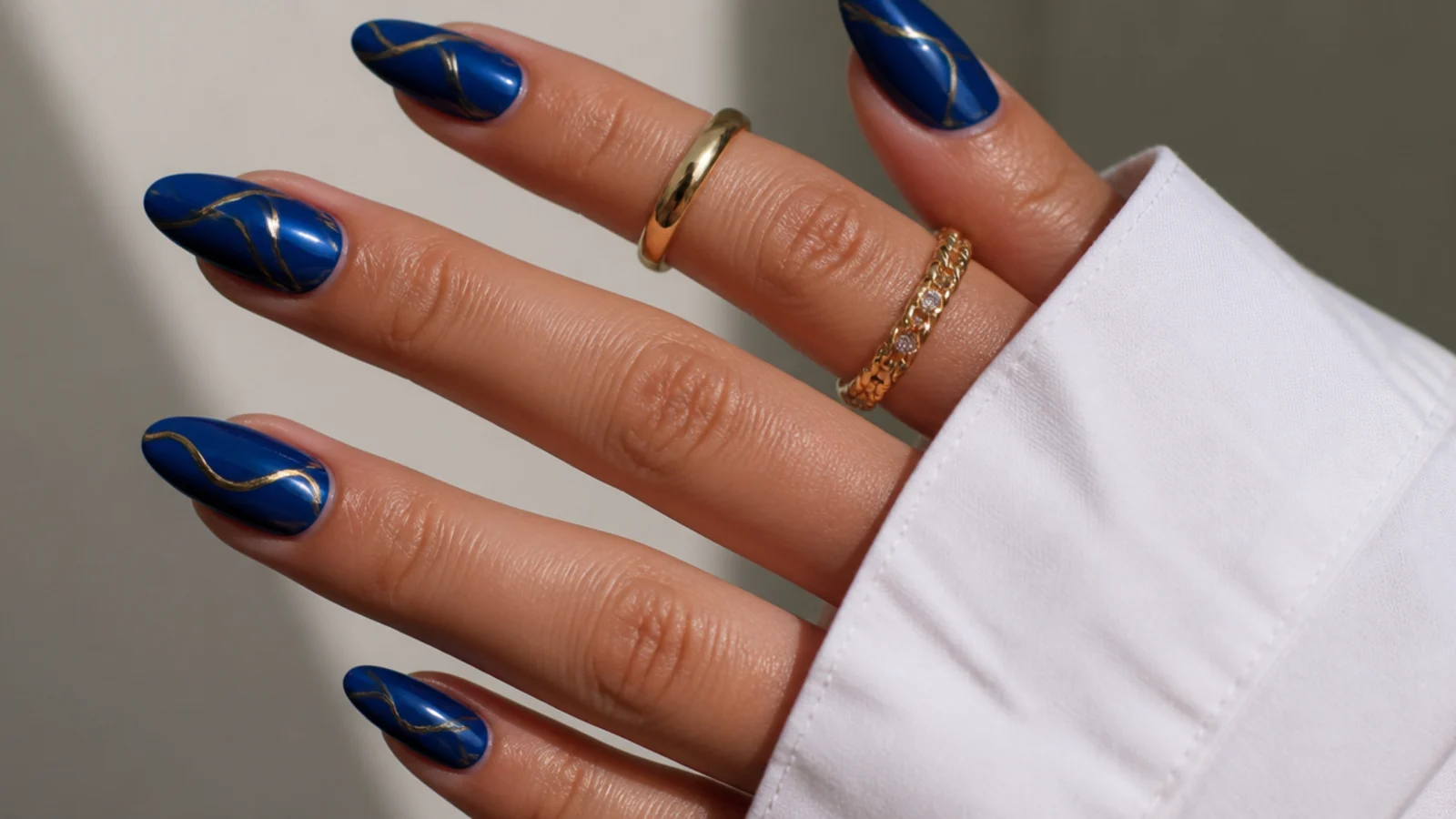 Royal blue acrylic nails with fine gold abstract line art on almond nails
