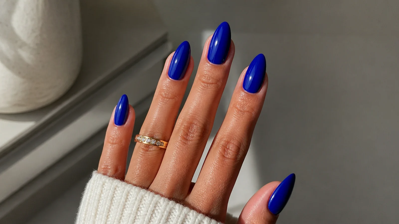 Bold royal blue acrylic nails in a glossy almond shape on medium skin