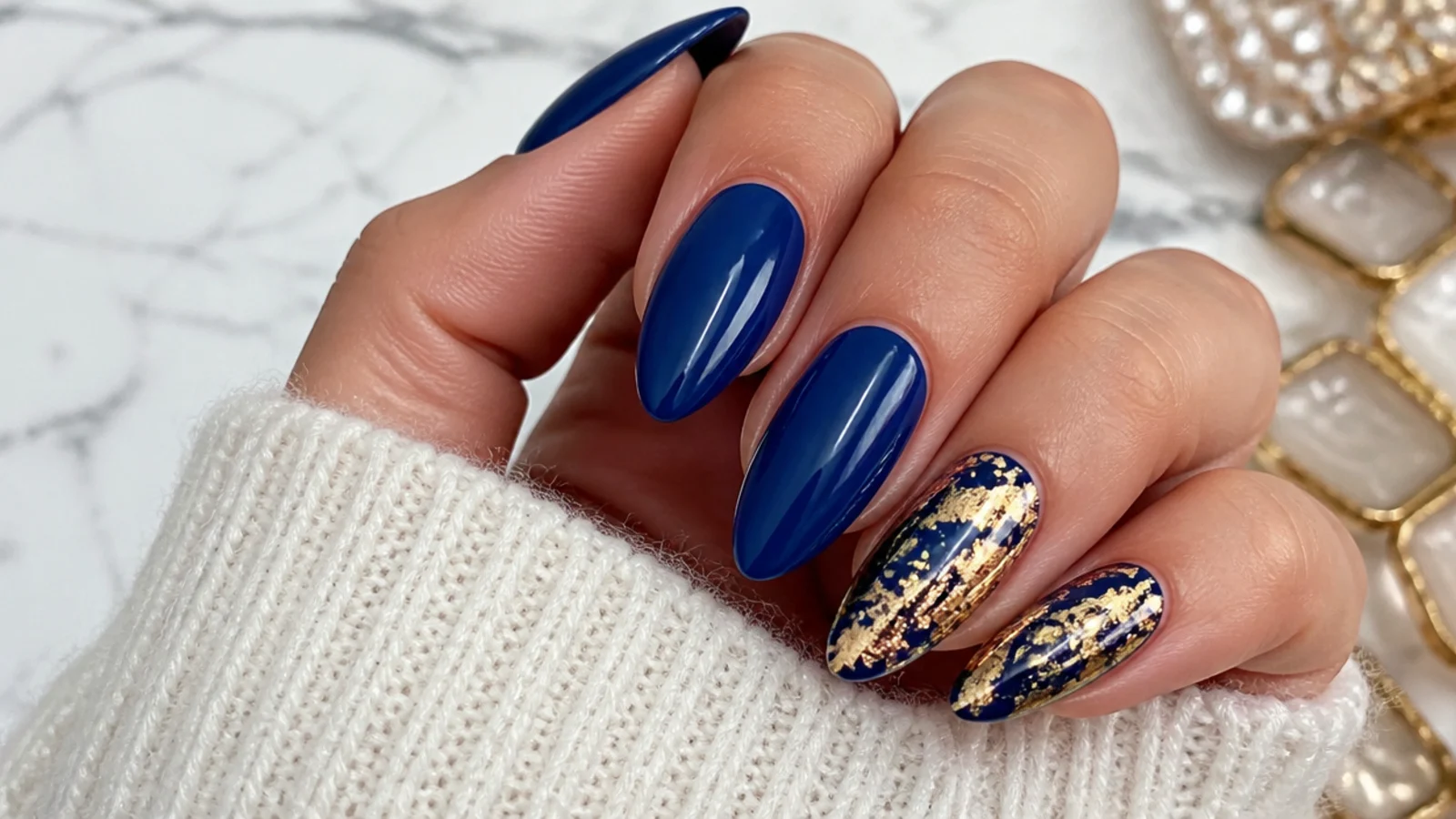 Royal blue almond nails with gold foil accents on two nails