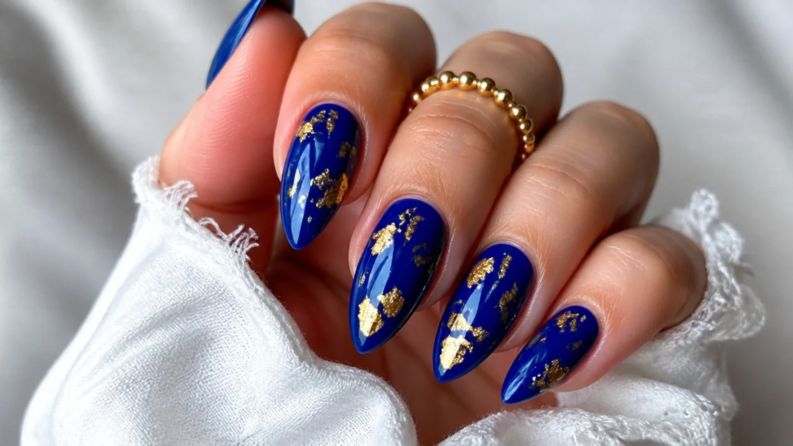Deep royal blue almond nails with scattered gold foil flecks