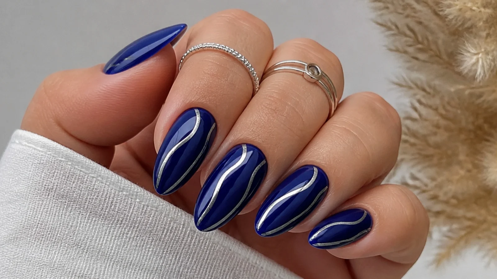 Royal blue almond nails with abstract silver chrome swirl accents