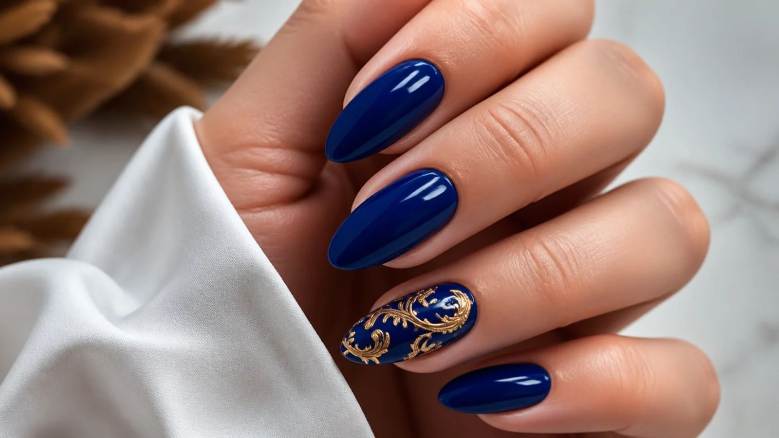 Royal blue nails with hand-drawn gold baroque swirls on an almond accent