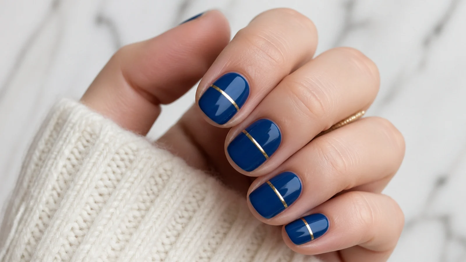 Short squoval royal blue nails with a single thin gold stripe each