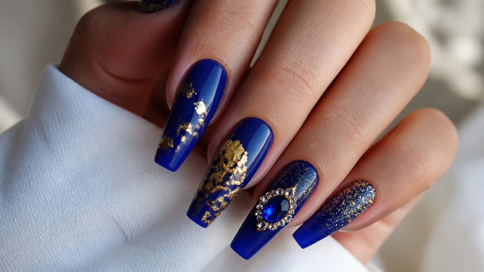 Long royal blue coffin nails mixing gold foil, glitter and a gem accent