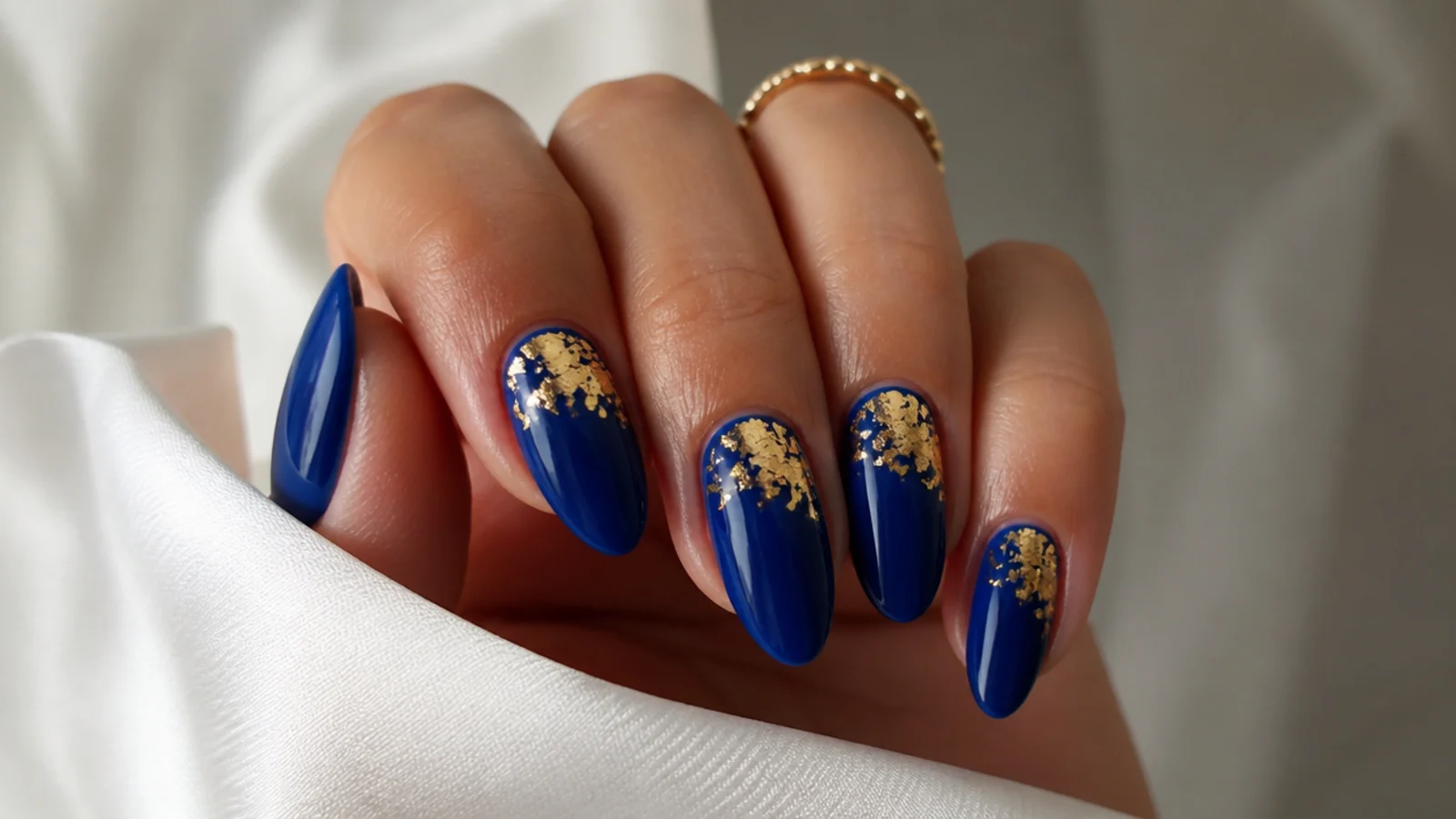 Glossy royal blue nails with gold foil accents on an almond shape