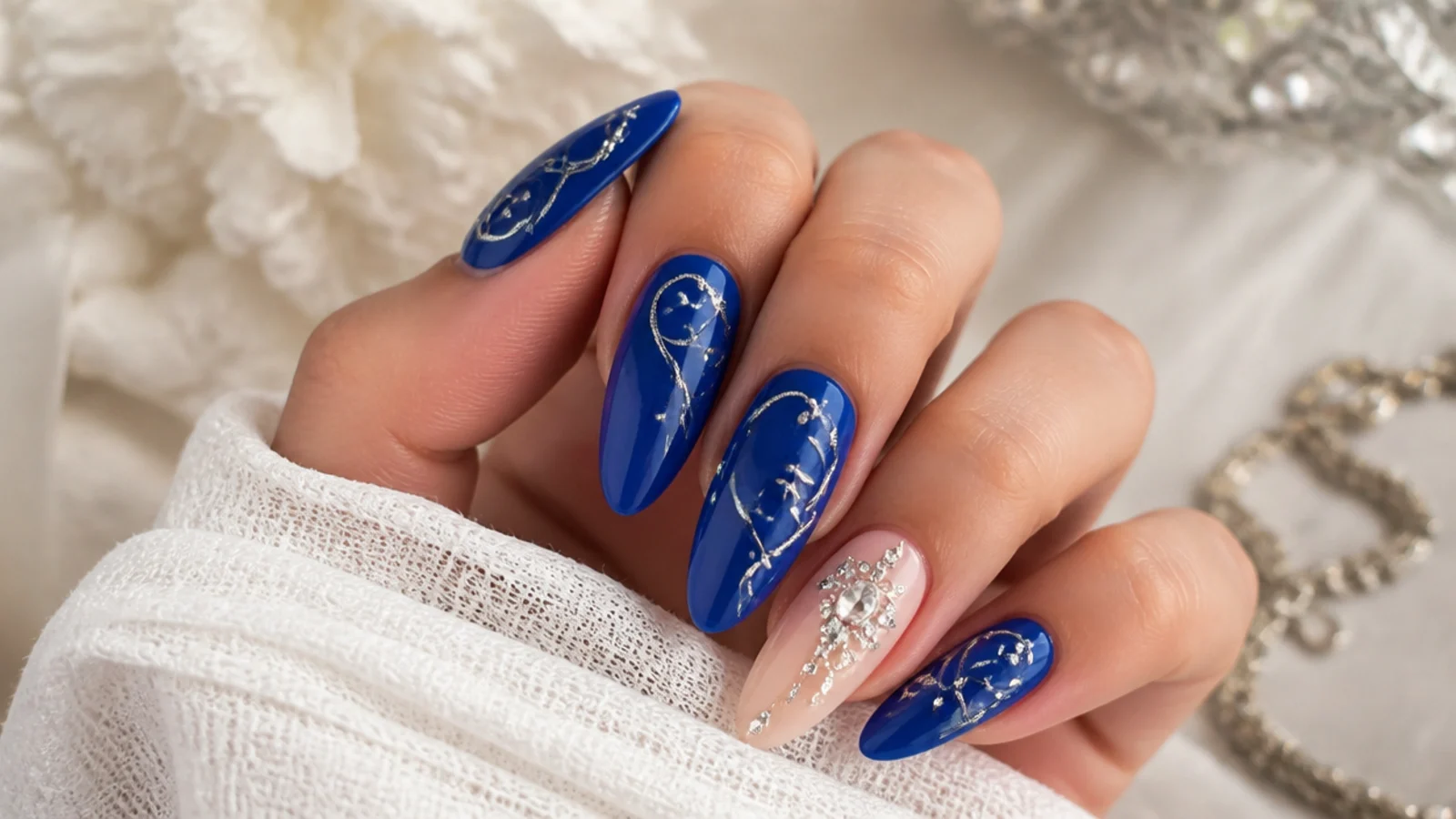 Royal blue almond nails with ornate silver swirls and rhinestones for a quinceanera