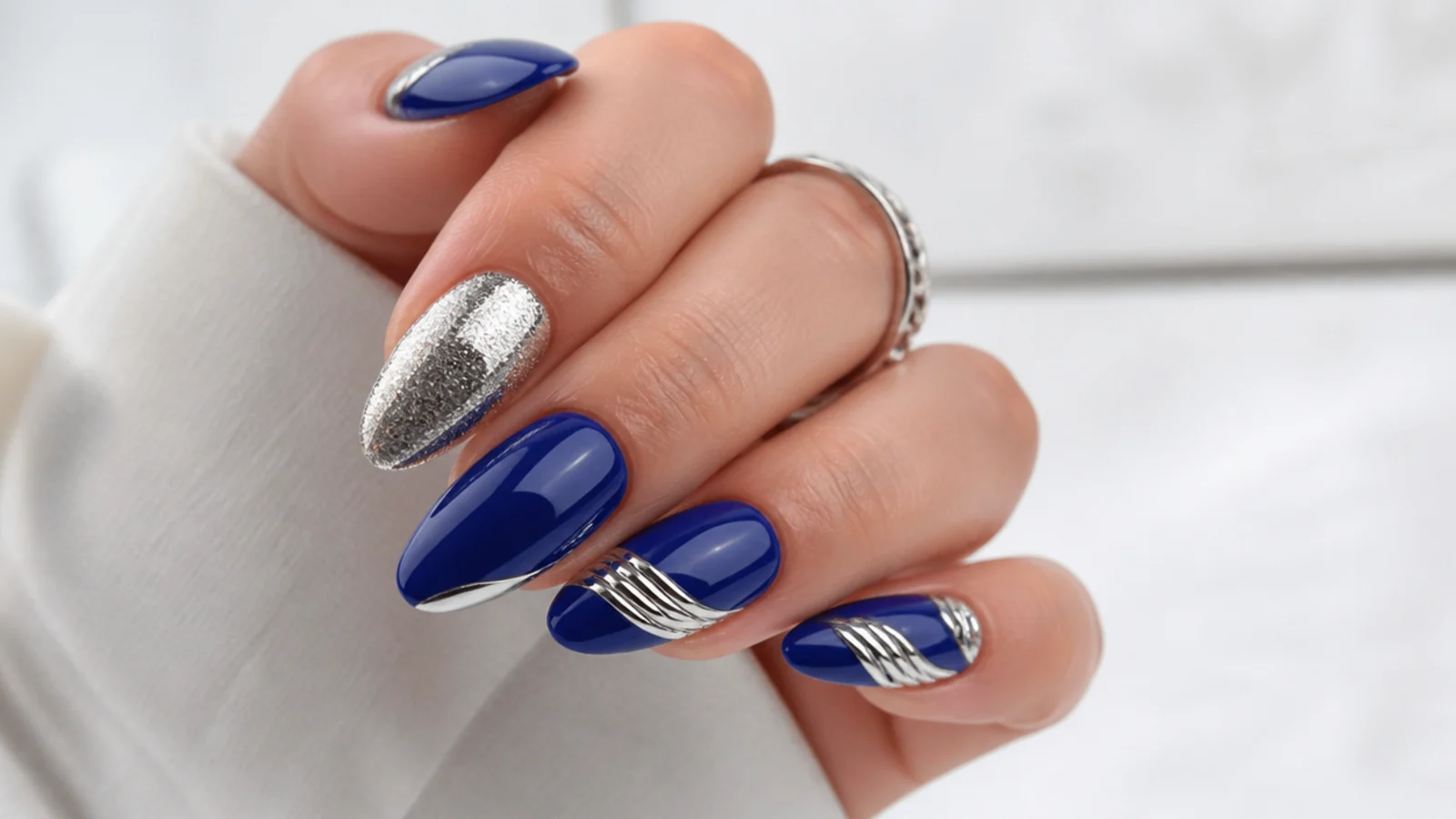 Glossy royal blue nails with silver chrome and glitter accents on an almond shape