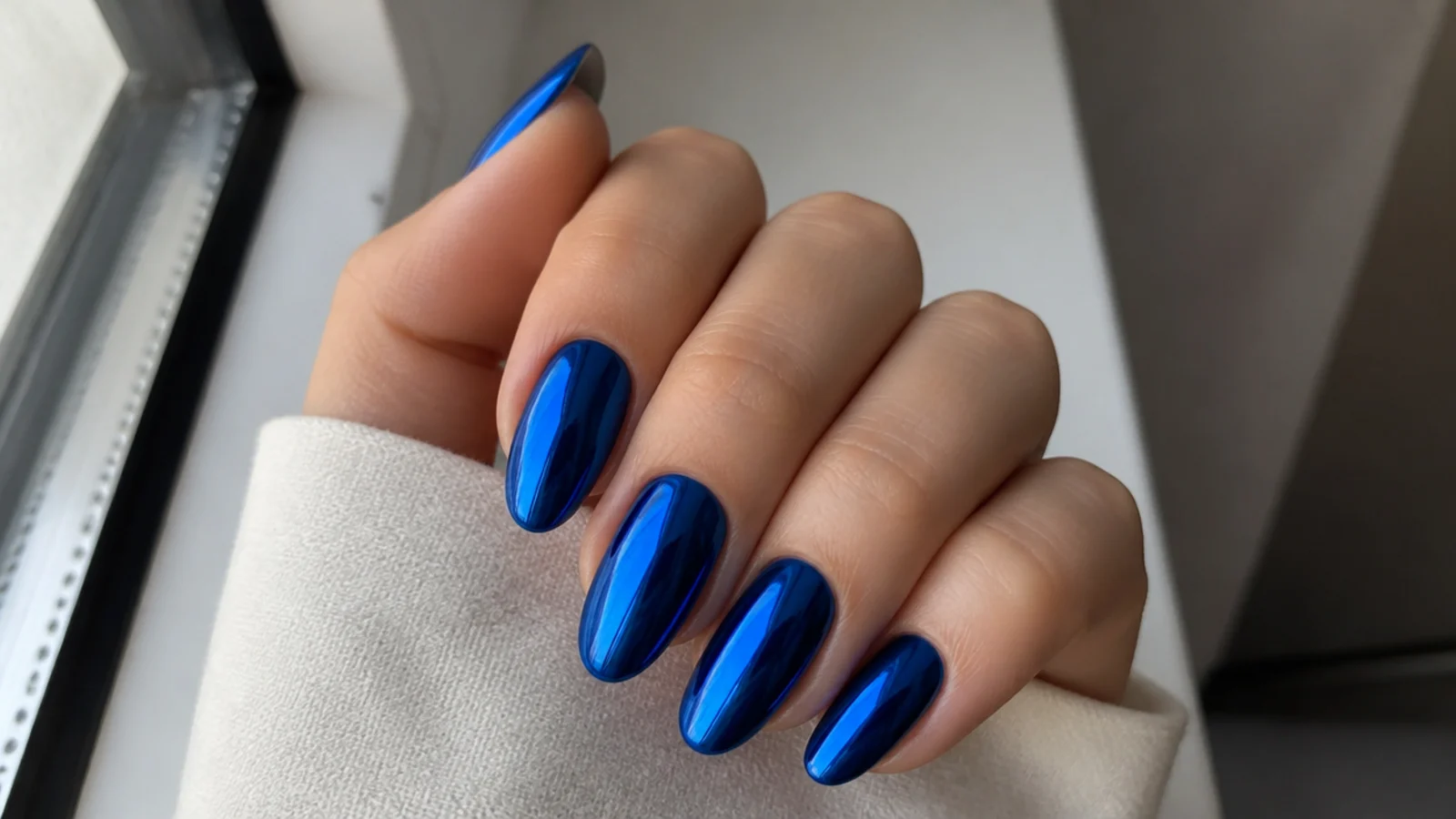 Mirror-finish royal blue chrome nails on an almond shape catching cool reflections