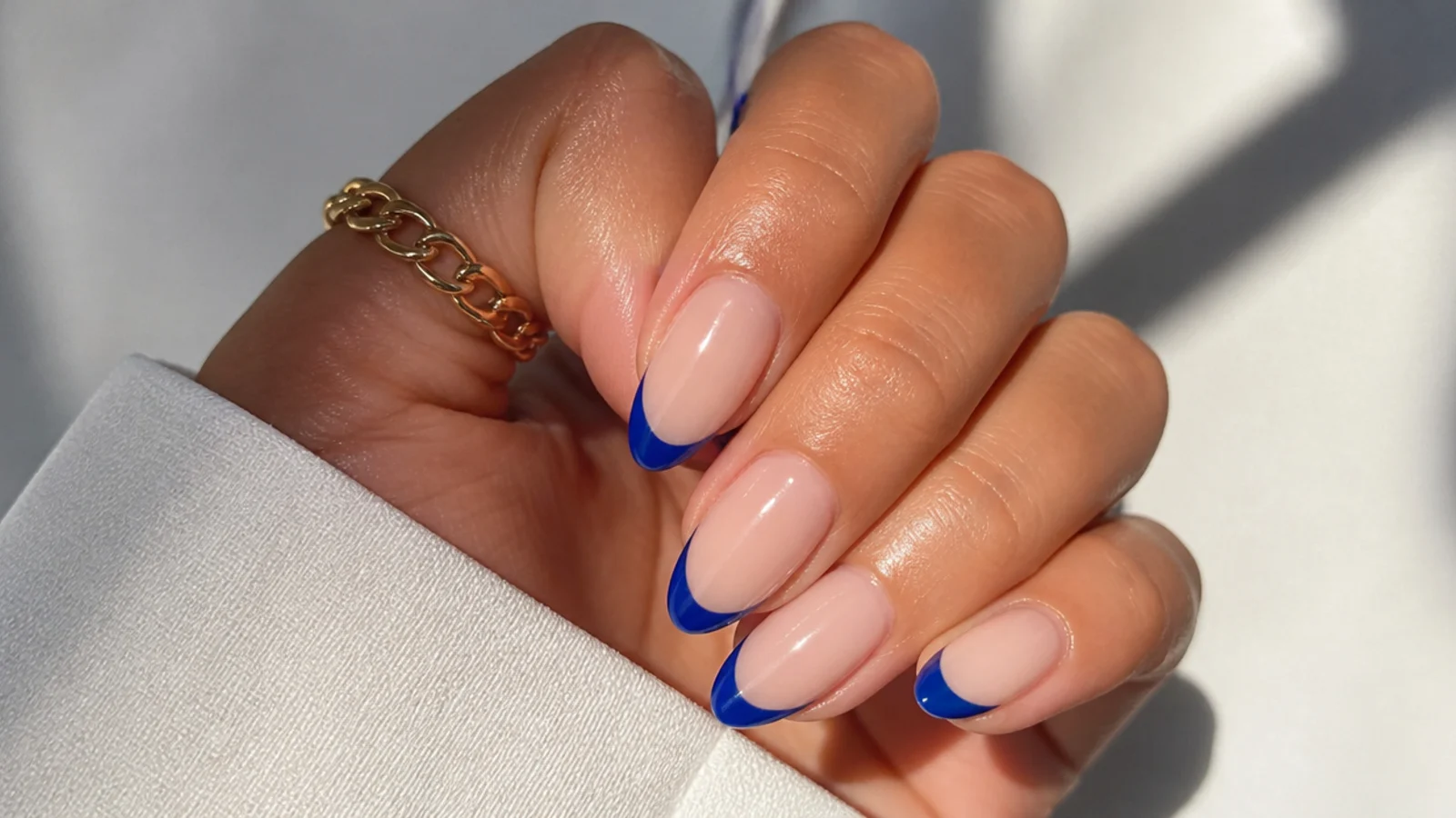 Nude nails with crisp royal blue french tips on an almond shape