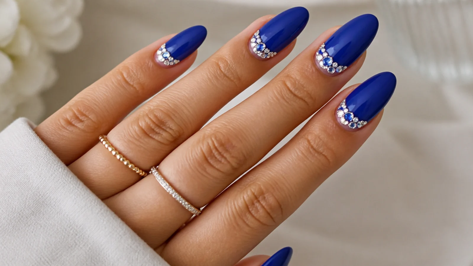 Royal blue nails with clustered clear and blue rhinestones near the cuticle