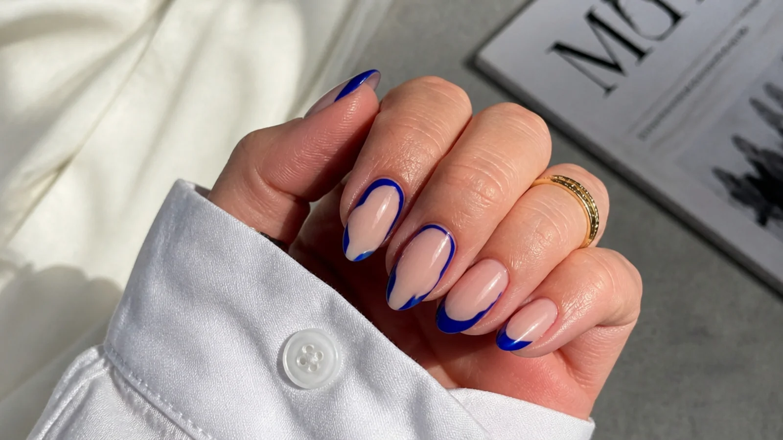 Almond nails with royal blue negative-space designs over bare nude nails