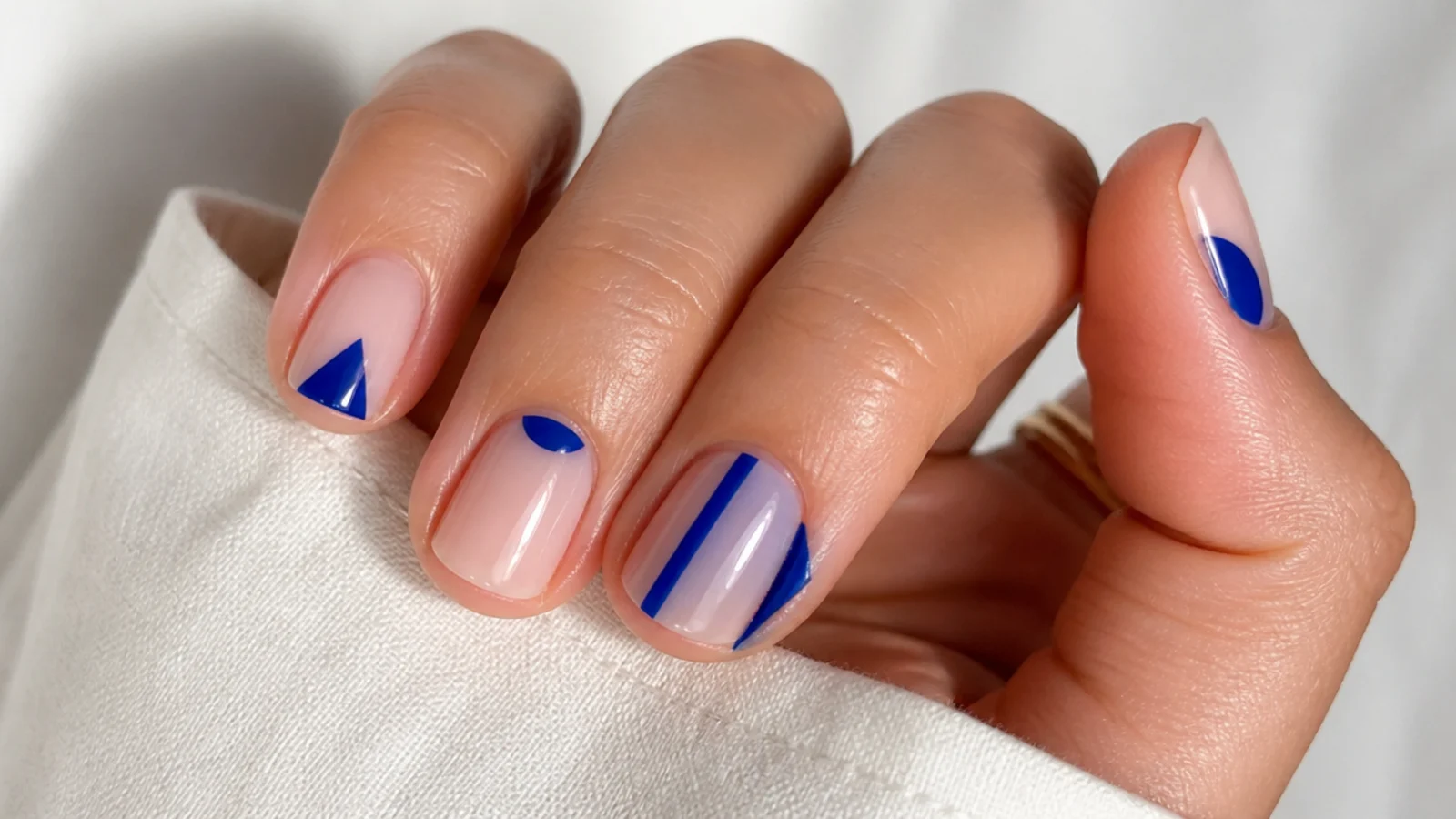 Short nails with royal blue geometric shapes over bare nude negative space