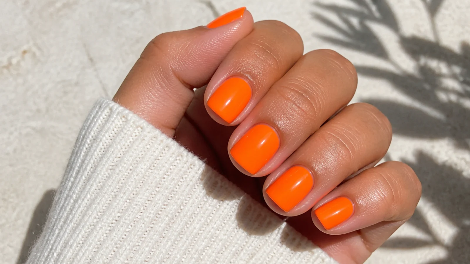 Short square nails in bright neon orange with opaque coverage against tanned skin