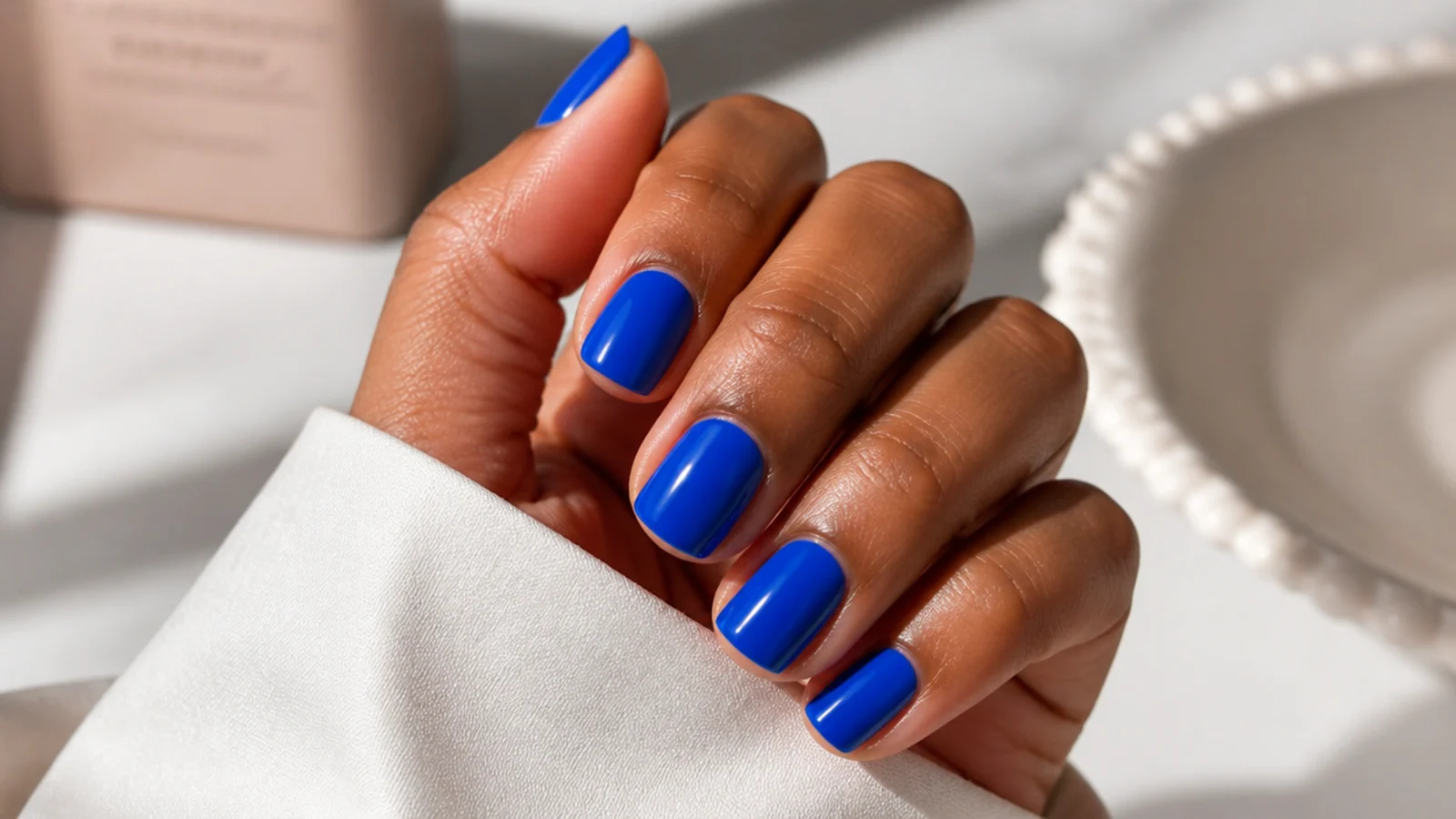 Short square nails on deep skin in a vivid royal blue cream with a glossy finish