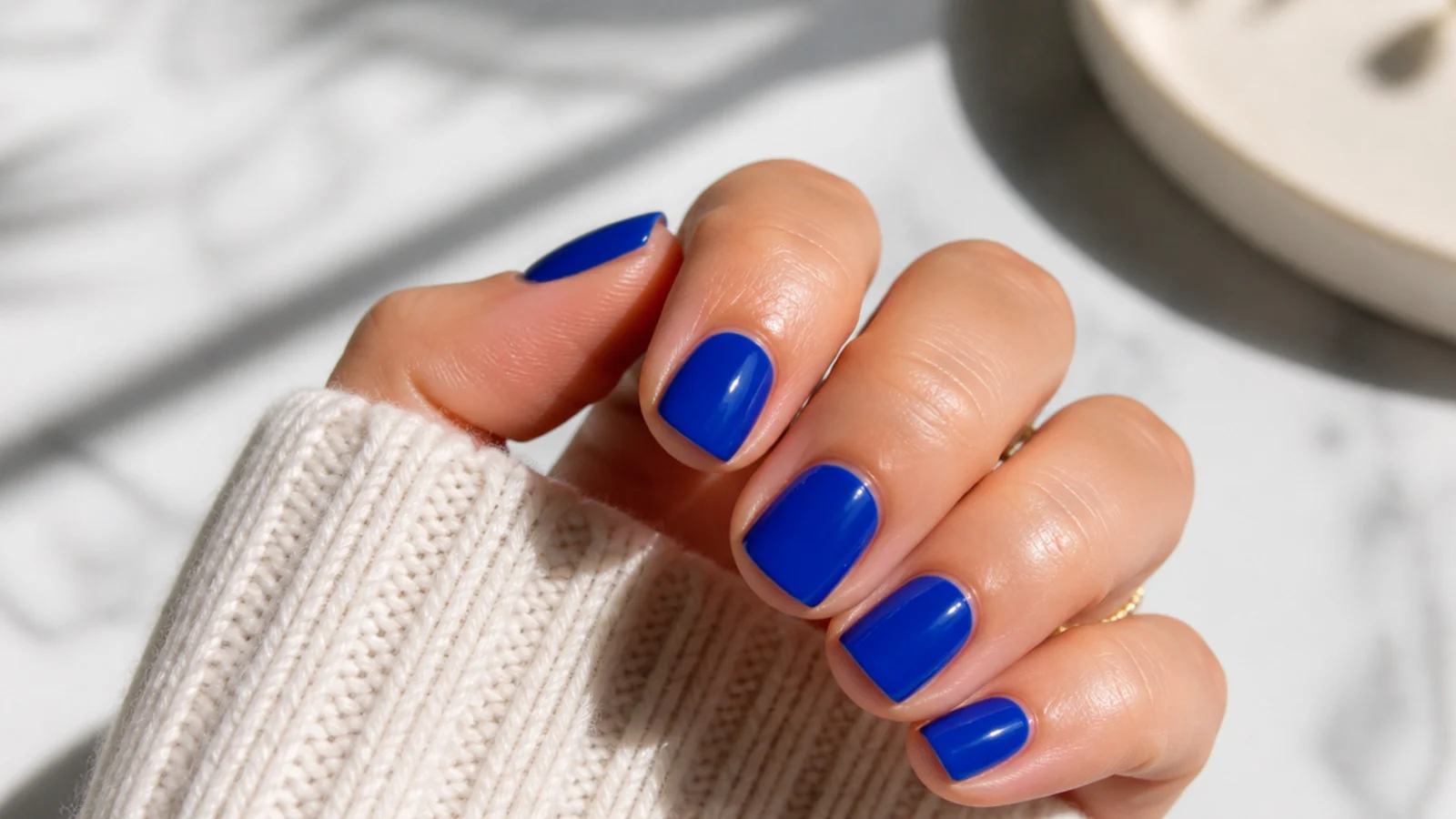 Short square nails in electric cobalt blue cream finish against a light background