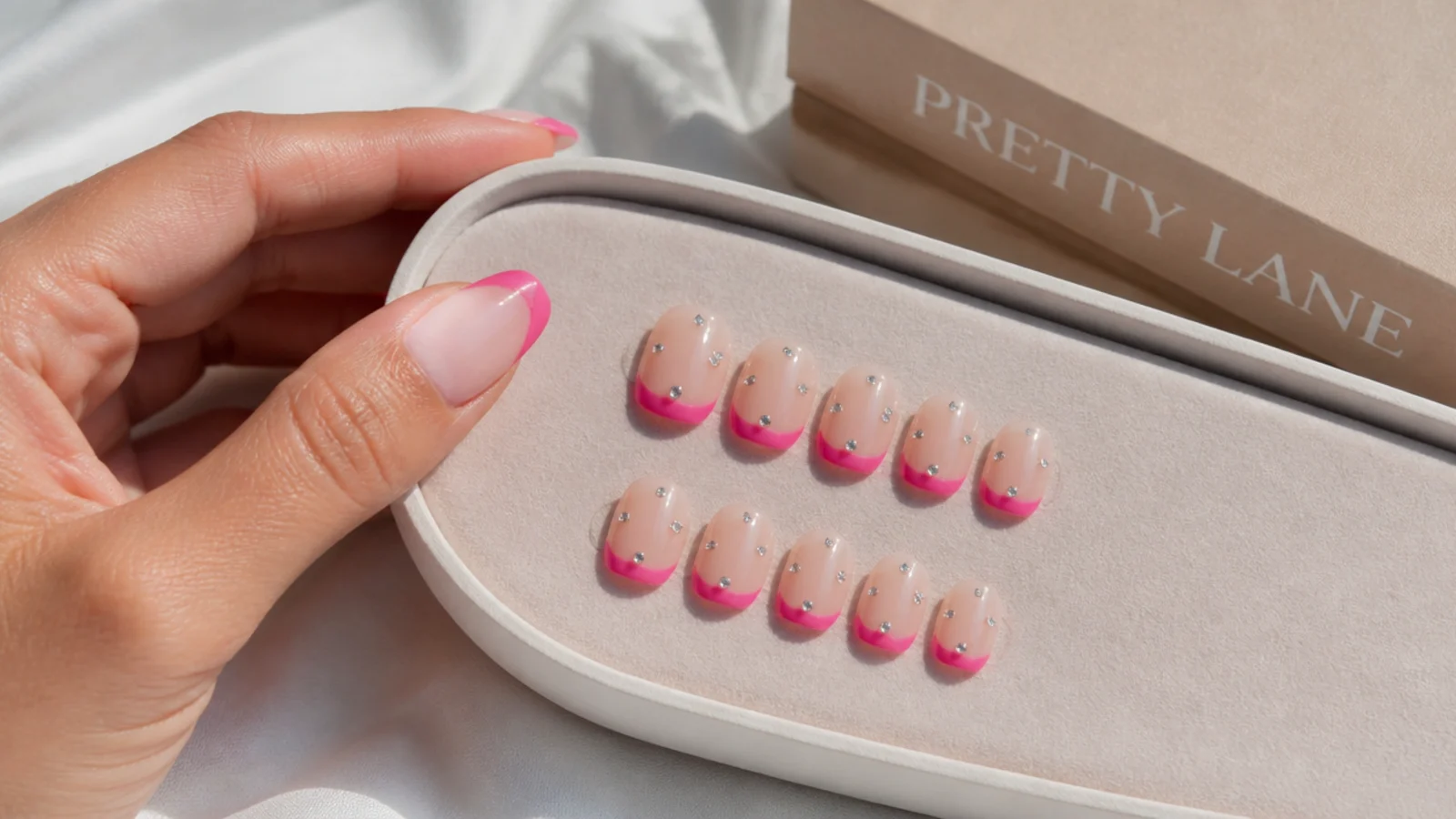 Set of short square press-on nails with hot pink French tips and rhinestones on a tray