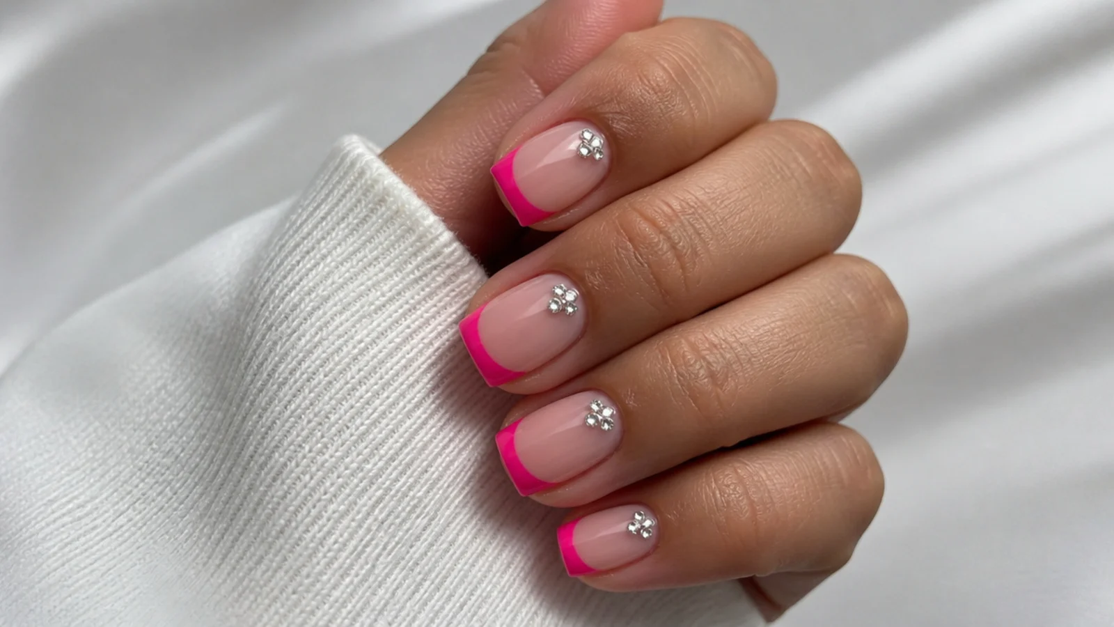 Short square baddie nails with hot pink French tips and a single rhinestone cluster near the cuticle