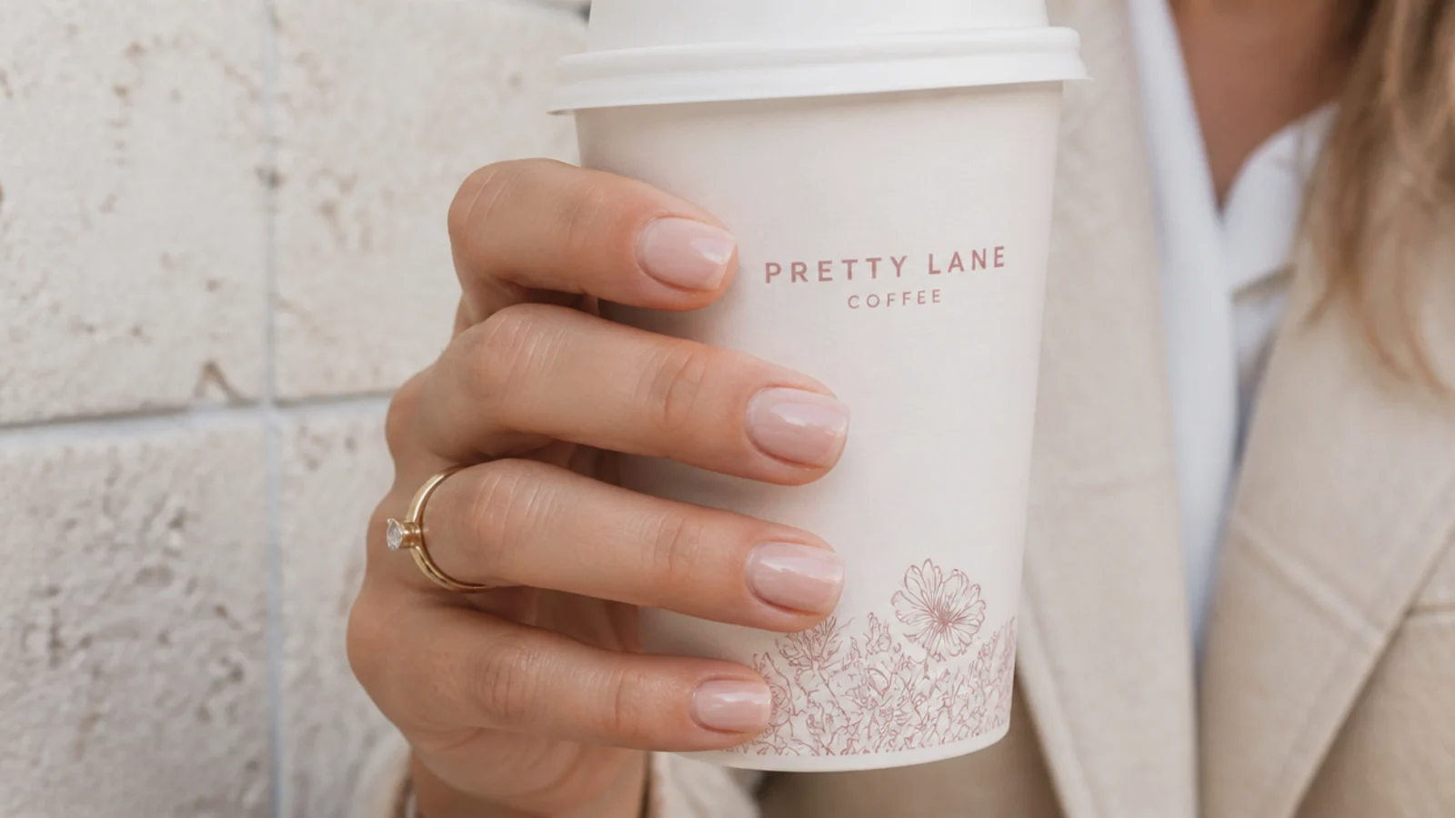 Short glossy squoval nails in a soft neutral shade holding a coffee cup