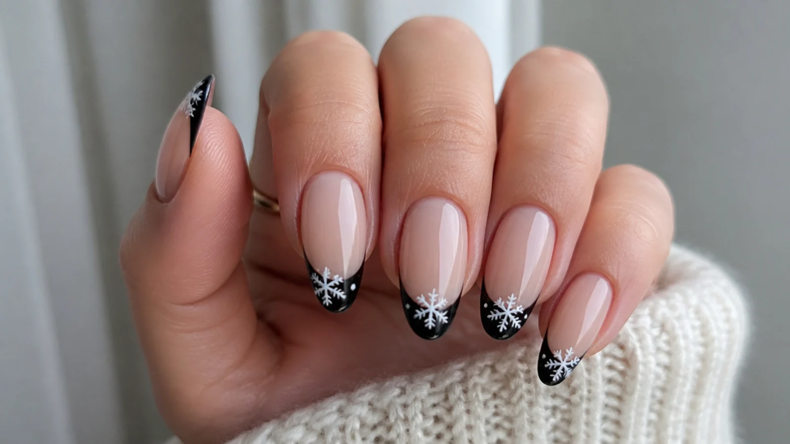 Nude nails with black French tips and small white snowflakes on the tips