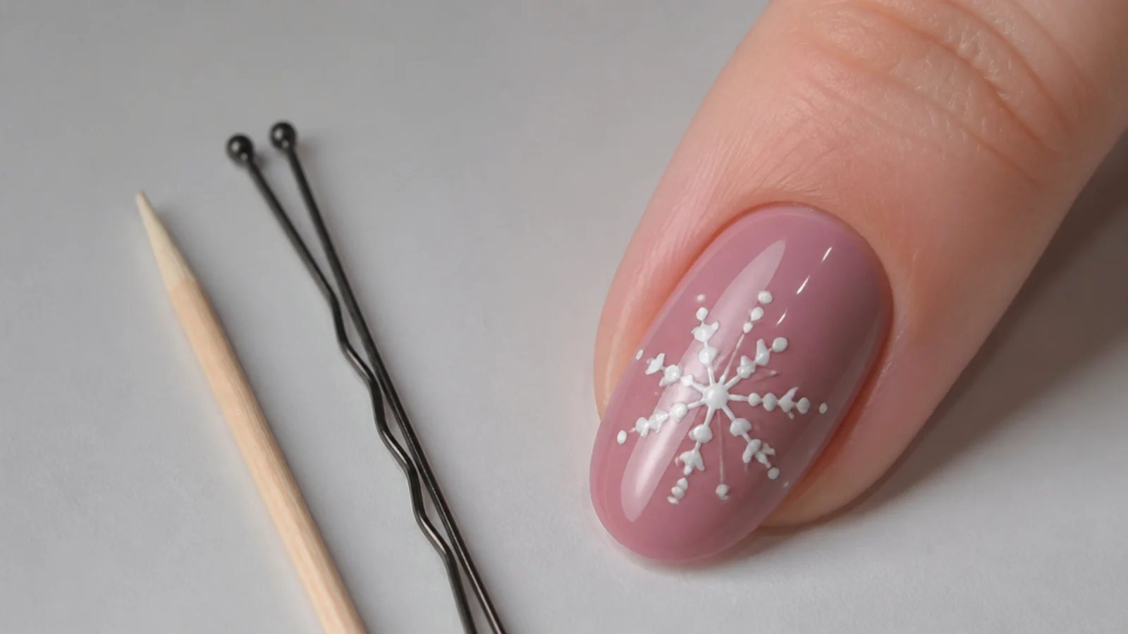 A toothpick and bobby pin next to a nail with a dotted snowflake