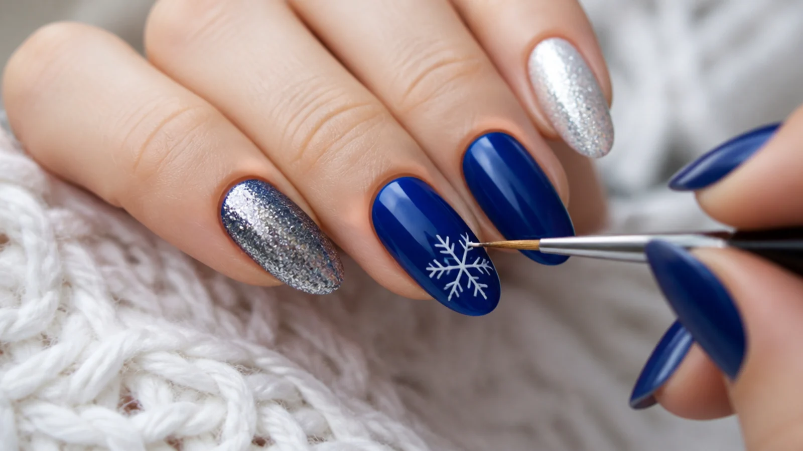 A fine detail brush drawing a six-point white snowflake on a blue nail