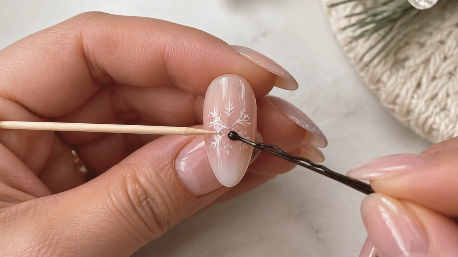 A toothpick and bobby pin dotting a white snowflake on a nail