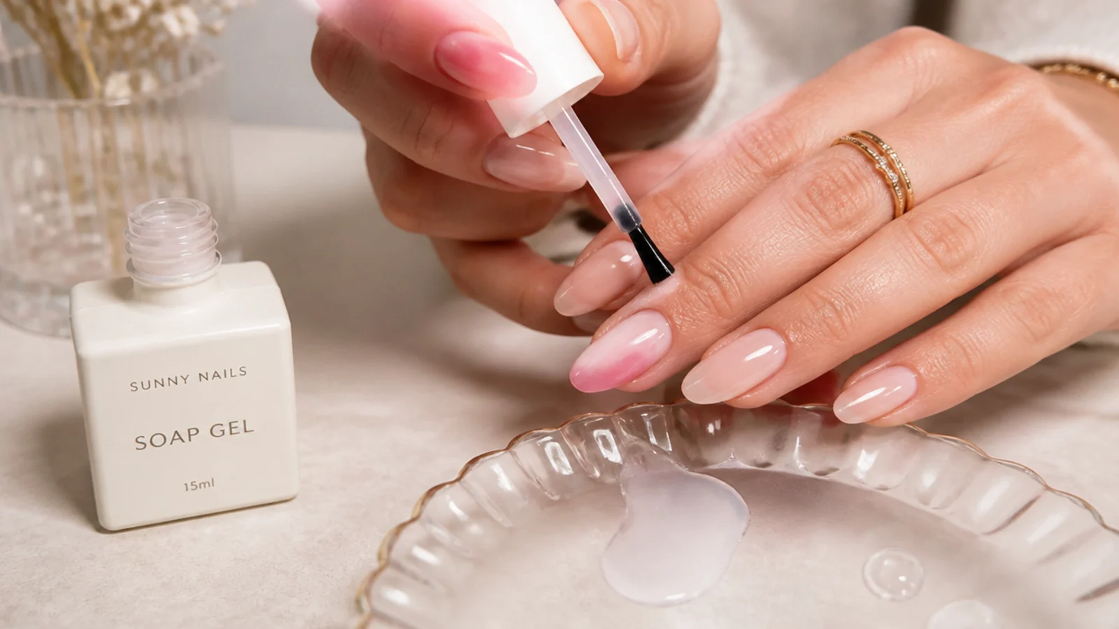 Hands mid-application of a sheer milky soap gel at a home nail setup