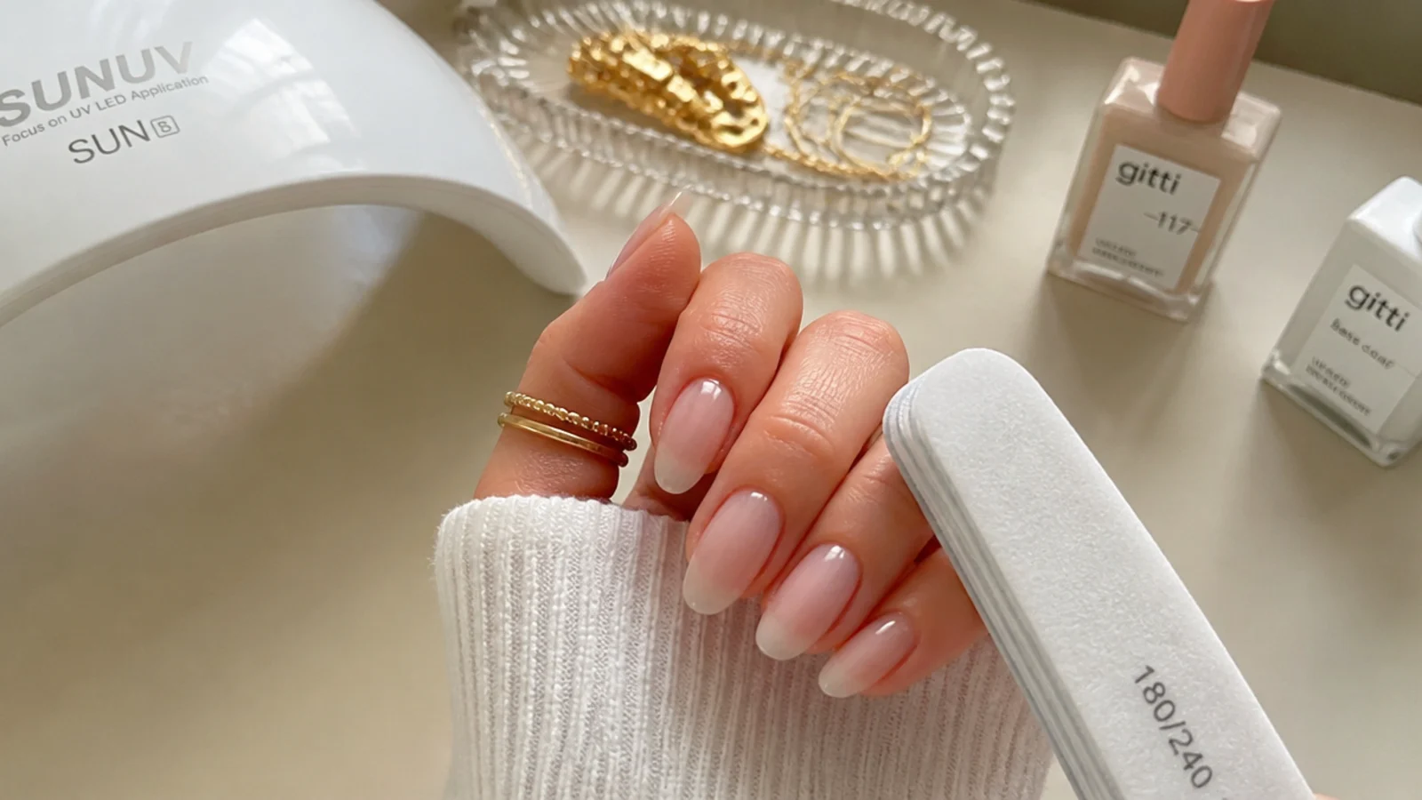 A home nail setup with sheer milky gel, a lamp and buffer mid-application