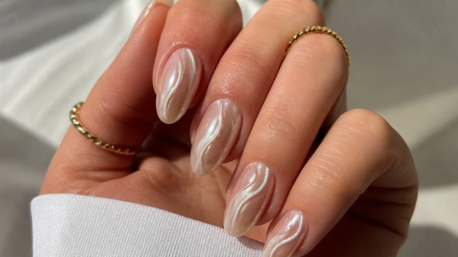 White chrome nails with a soft pearl swirl over a sheer nude base