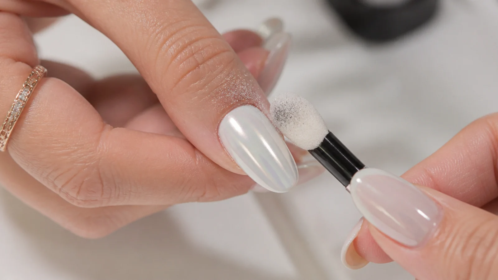 Chrome powder being buffed over a cured milky-white gel nail with an applicator
