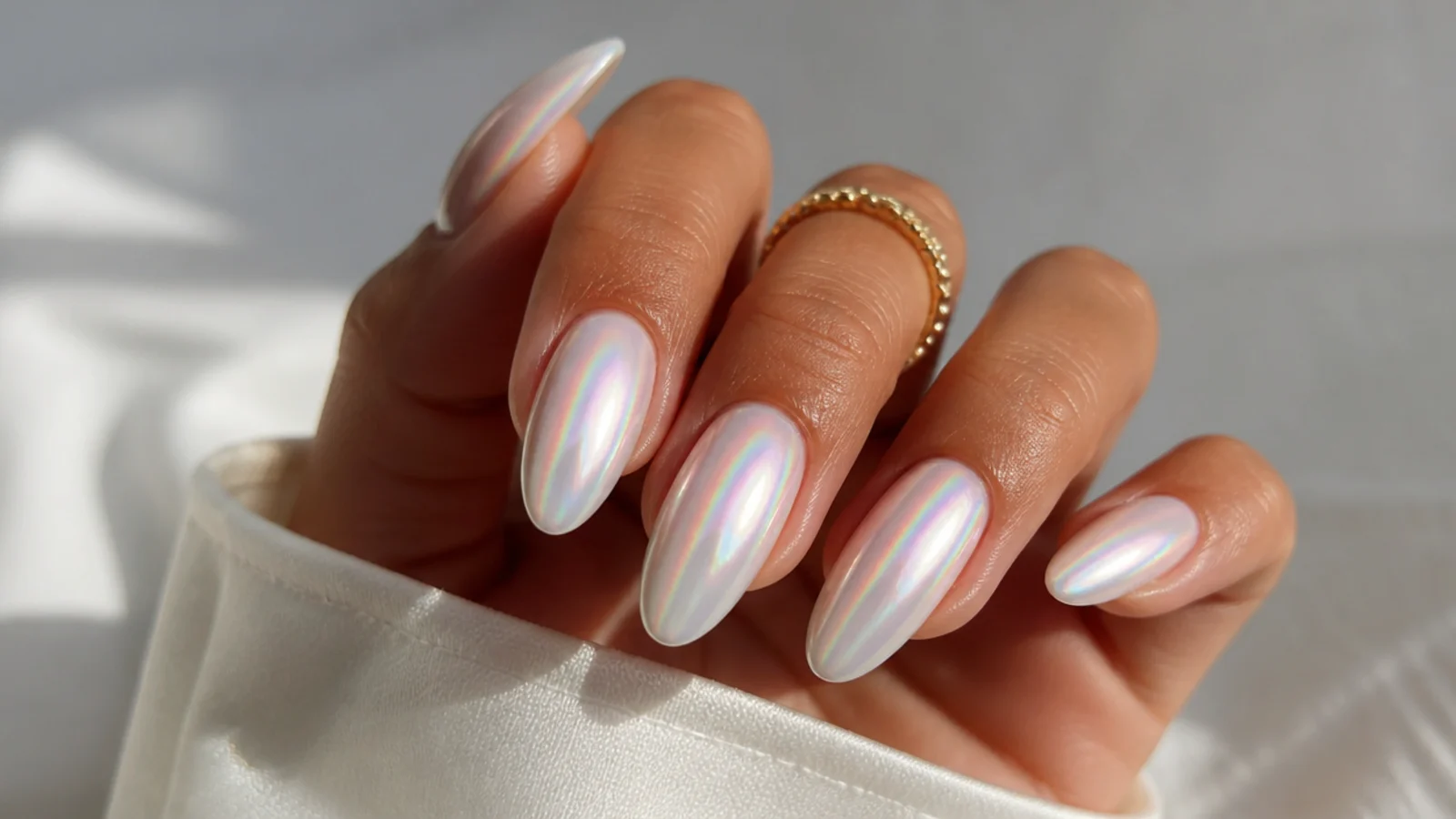 Pearl white chrome nails with a rainbow aurora shimmer on almond nails