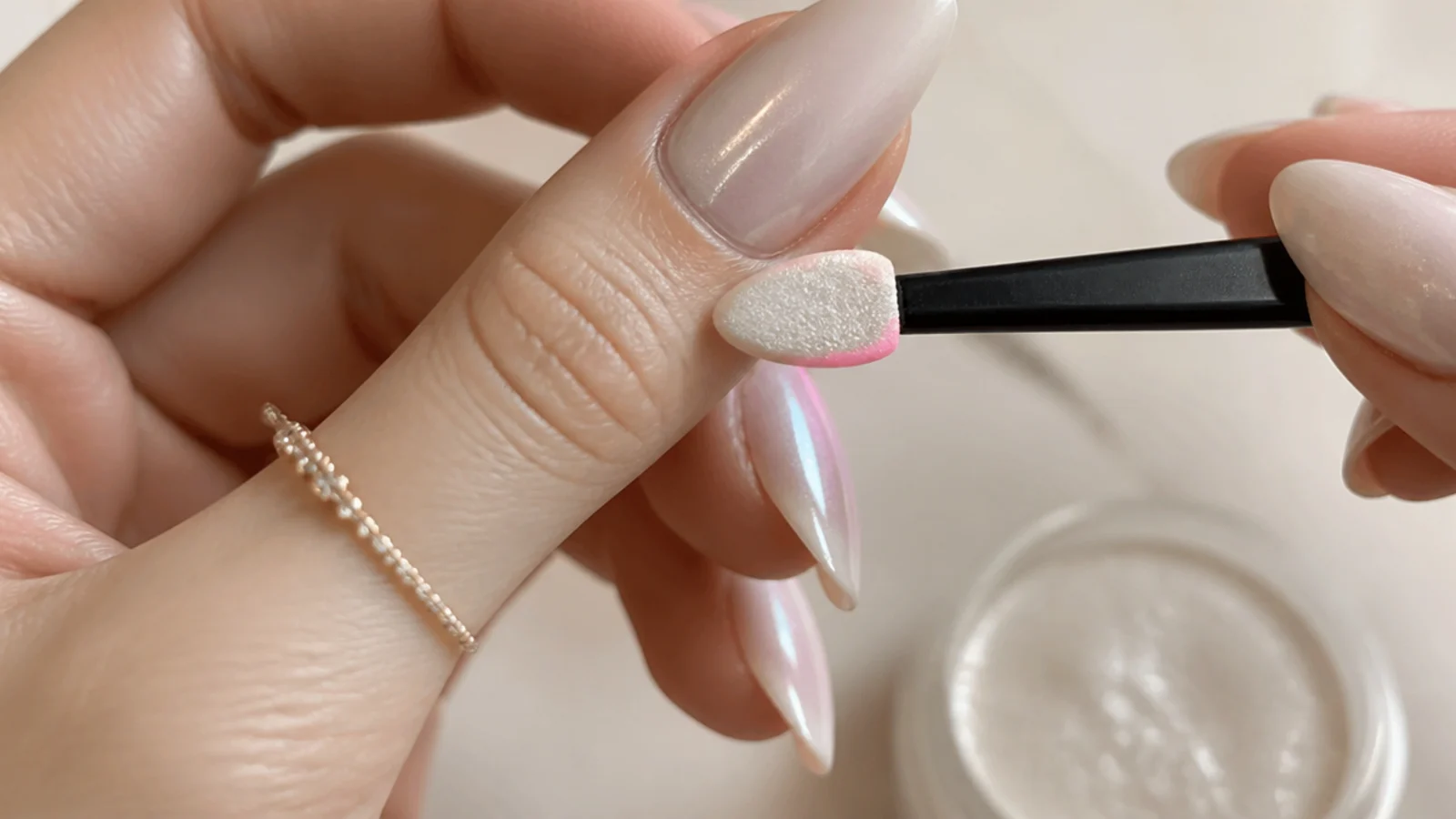 Pearl chrome powder being buffed onto a milky gel nail with an applicator