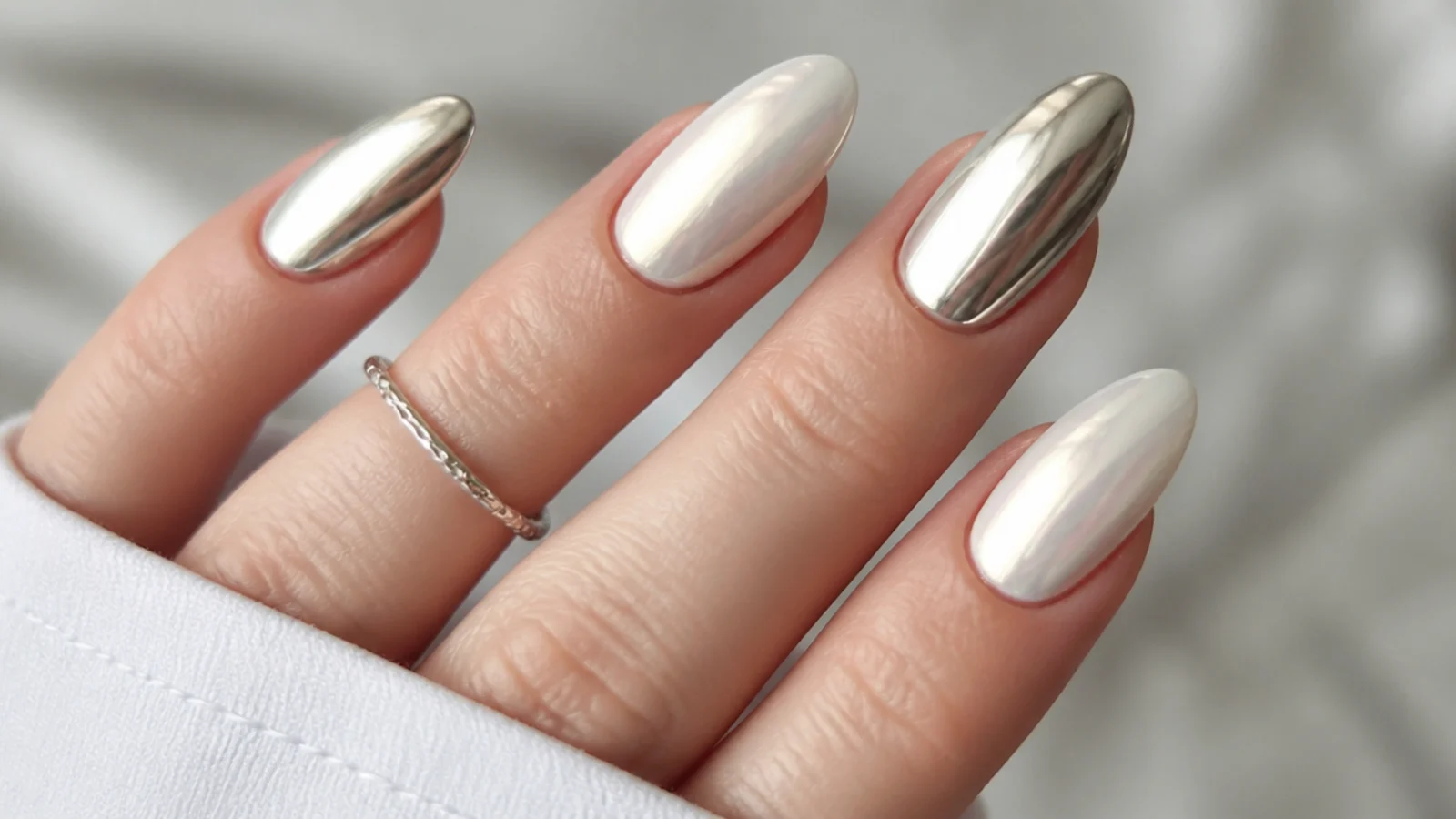 Soft milky white pearl chrome nail beside a bright silver mirror chrome nail