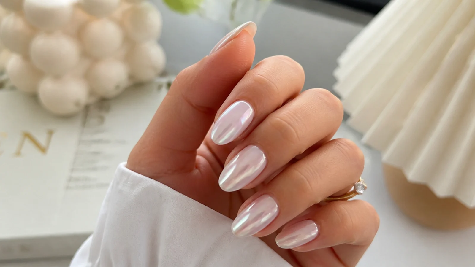 A hand of glassy white chrome nails with a soft pearl glazed-donut glow at home