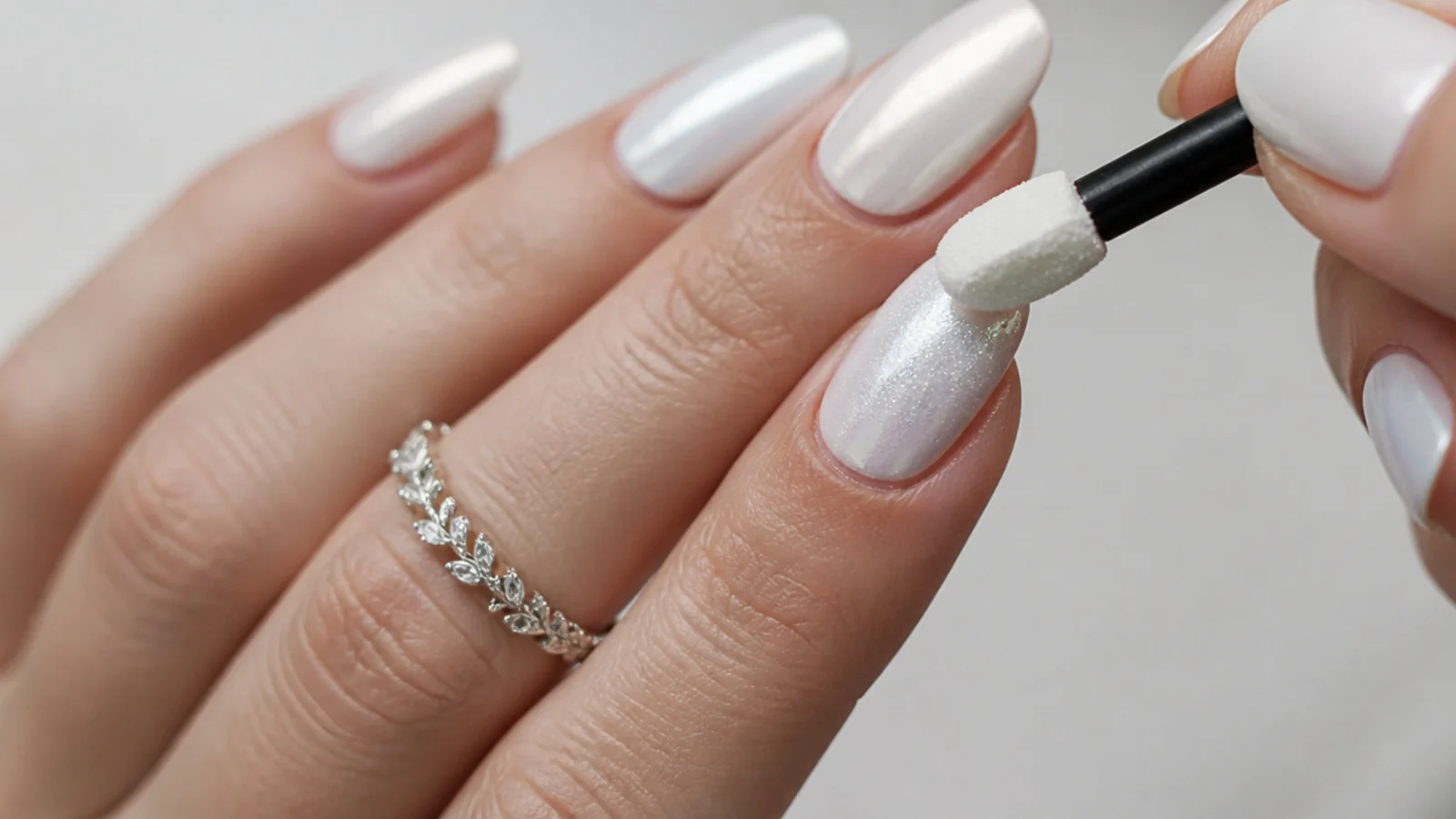 Chrome powder being buffed over a cured white gel nail with an applicator