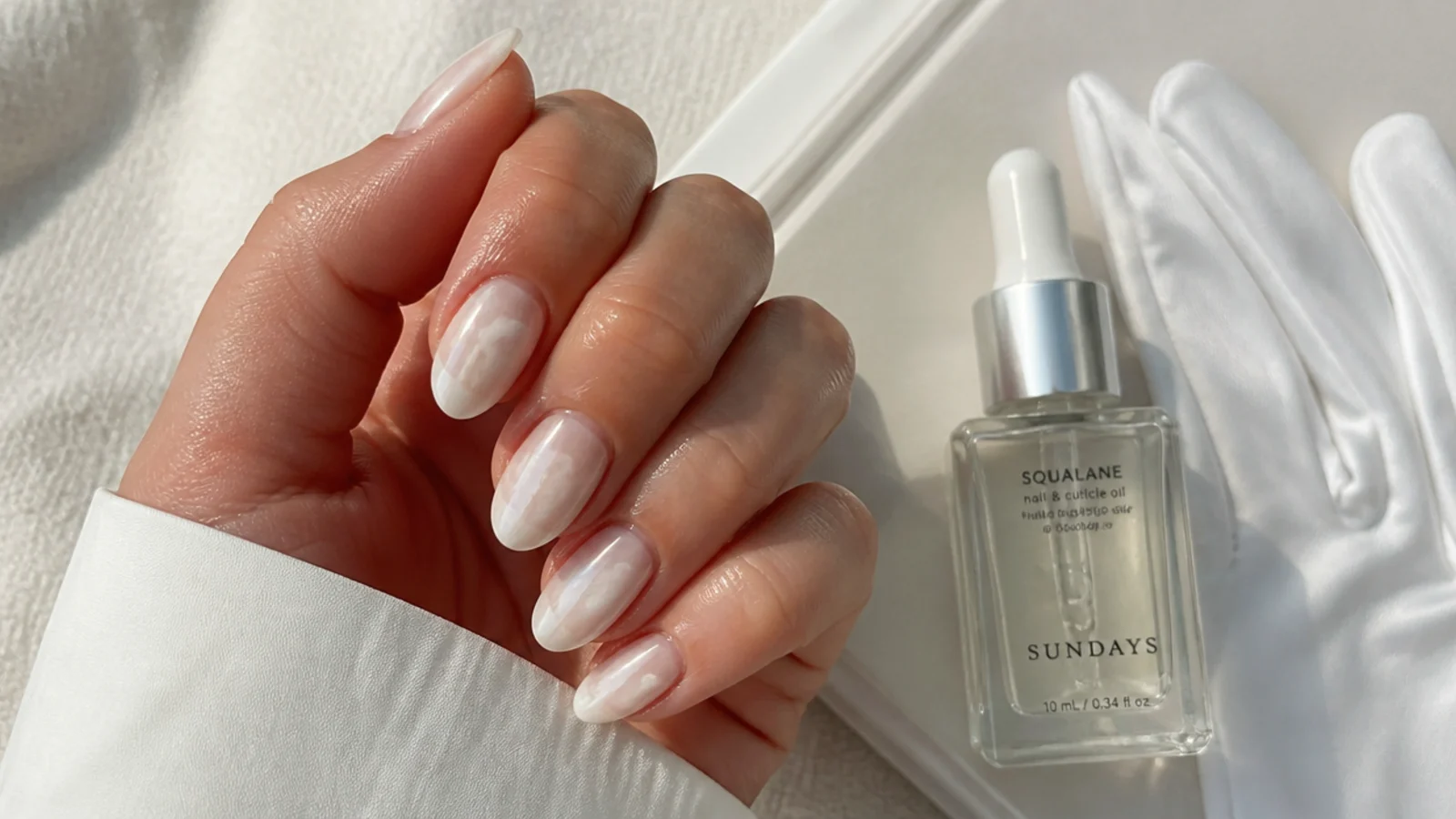 Cloudy dulled white chrome nails beside cuticle oil and gloves for aftercare