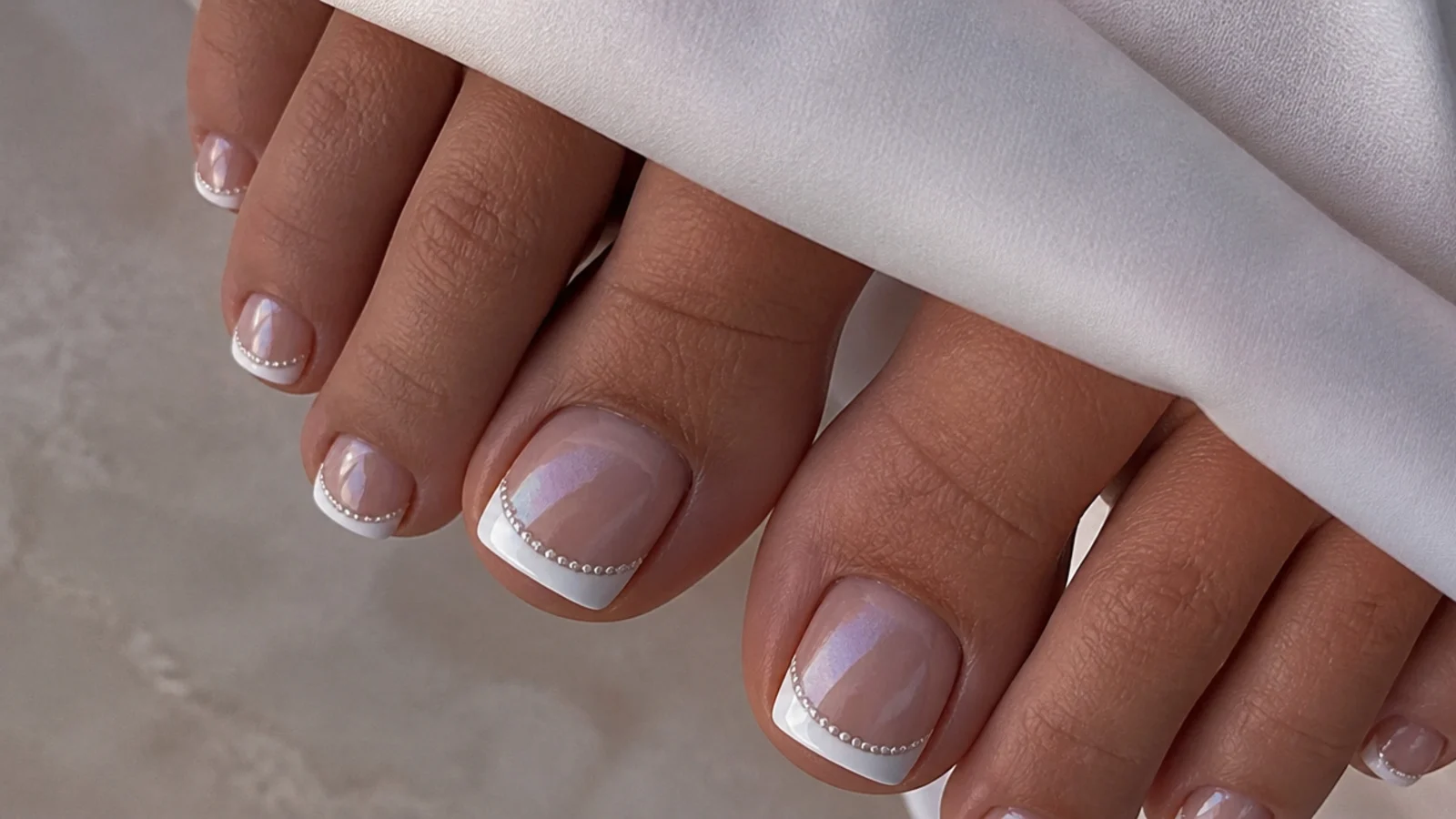 White chrome French tip toe nails with a pearl glazed smile line