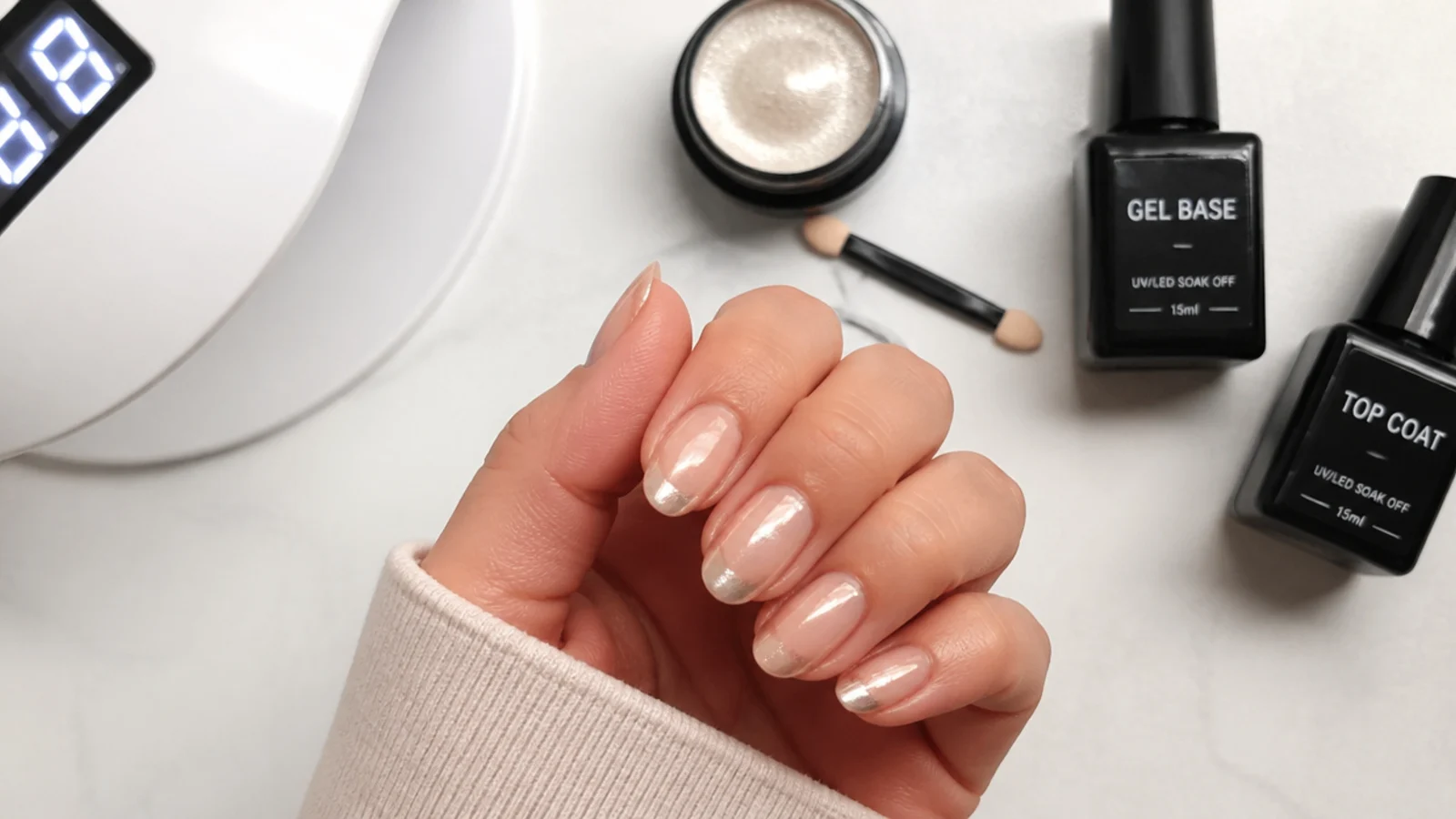 Flat lay of gel base, milky color, chrome powder, applicator, lamp and top coat