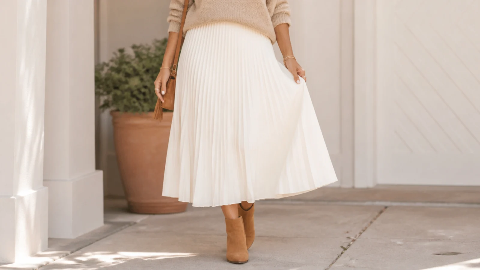Faceless outfit with a white pleated midi skirt and cognac suede ankle boots at the hem
