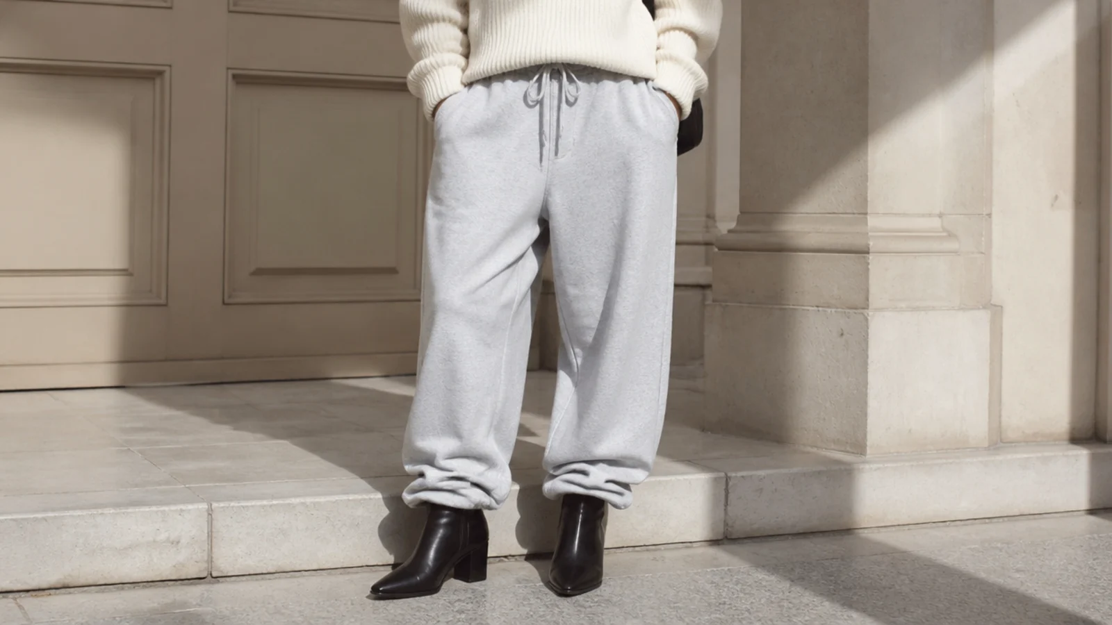 Faceless waist-down shot of sleek black leather ankle boots with baggy gray sweatpants stacked at the hem