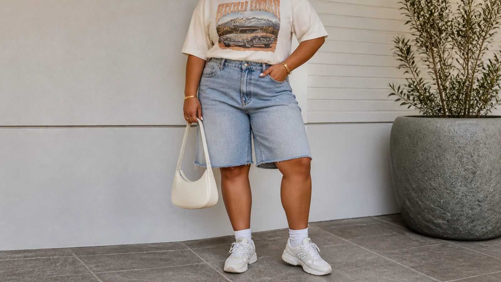 Faceless curvy outfit with baggy light-wash denim jorts, a boxy vintage graphic tee front-tucked and chunky white sneakers