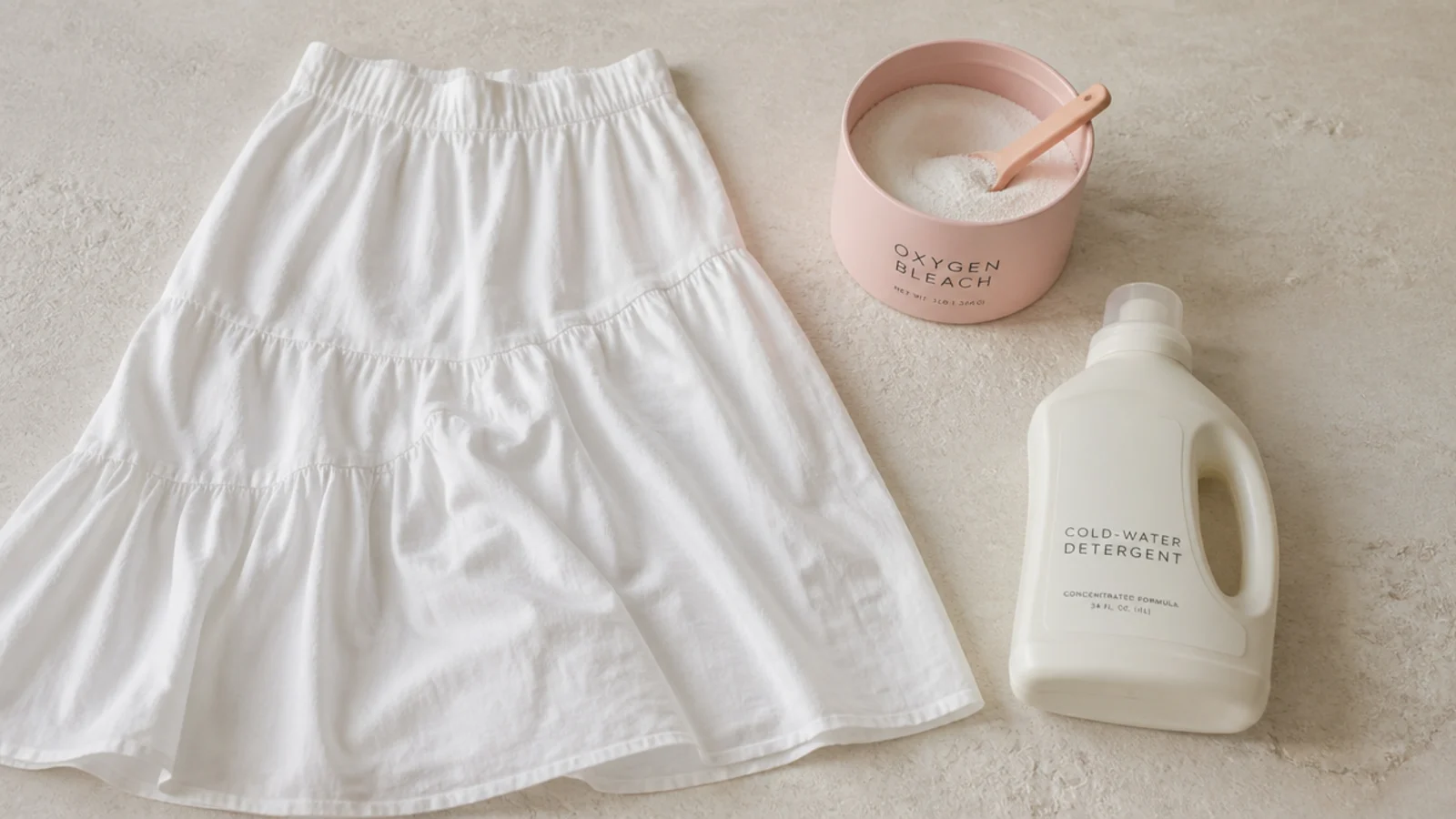 Faceless flat-lay of a white cotton skirt beside a scoop of oxygen bleach and cold-water detergent