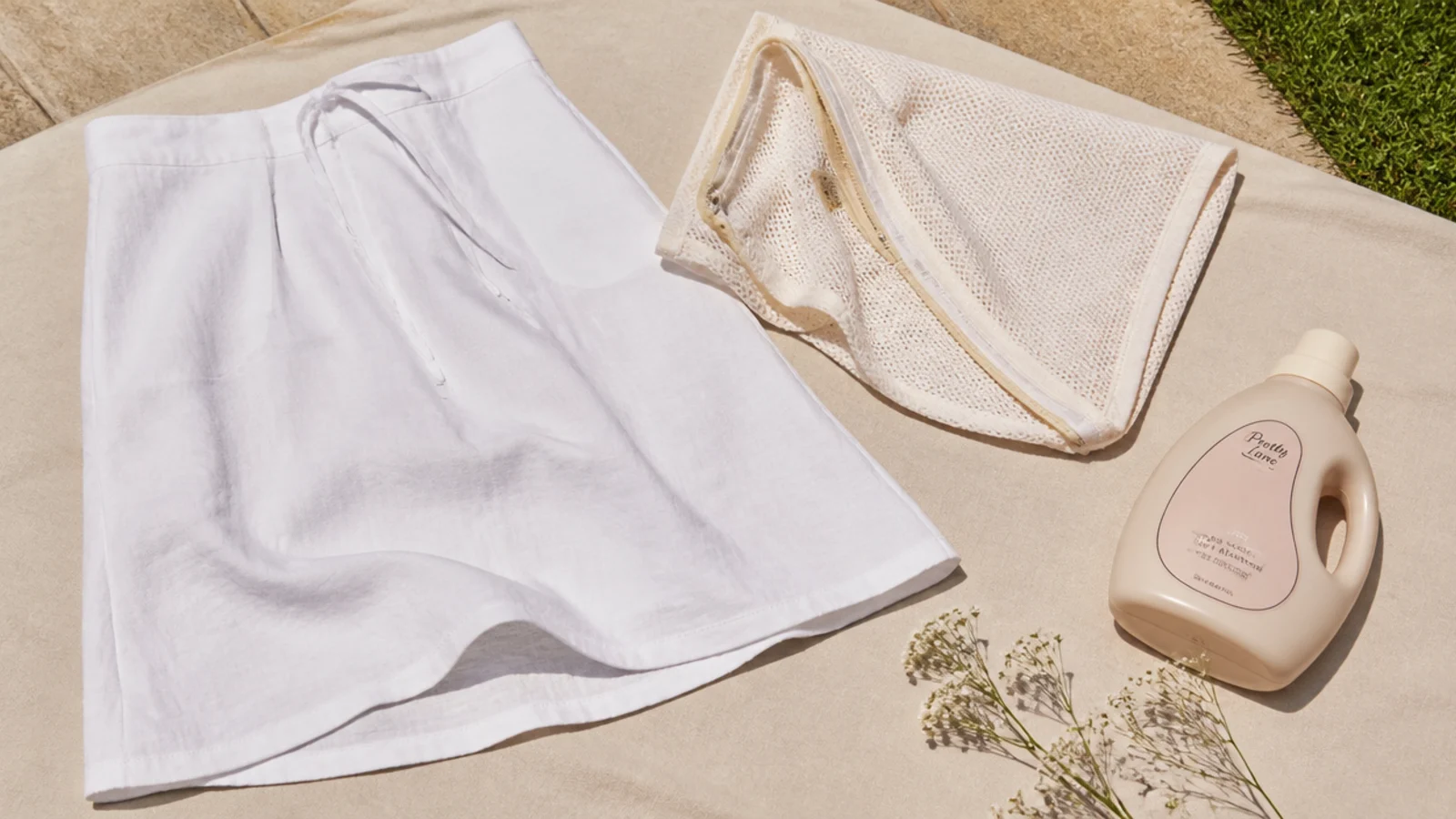 Faceless flat-lay of a white linen skirt laid flat to dry next to a mesh wash bag and mild detergent