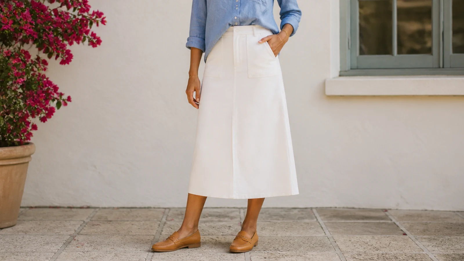 Faceless waist-down shot of a white midi skirt with a chambray shirt half-tucked and tan loafers