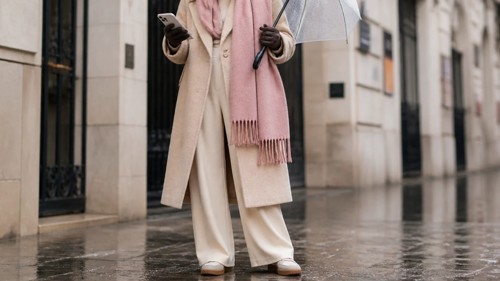 Faceless hands in slim waterproof touchscreen gloves holding a phone and an umbrella in cold rain