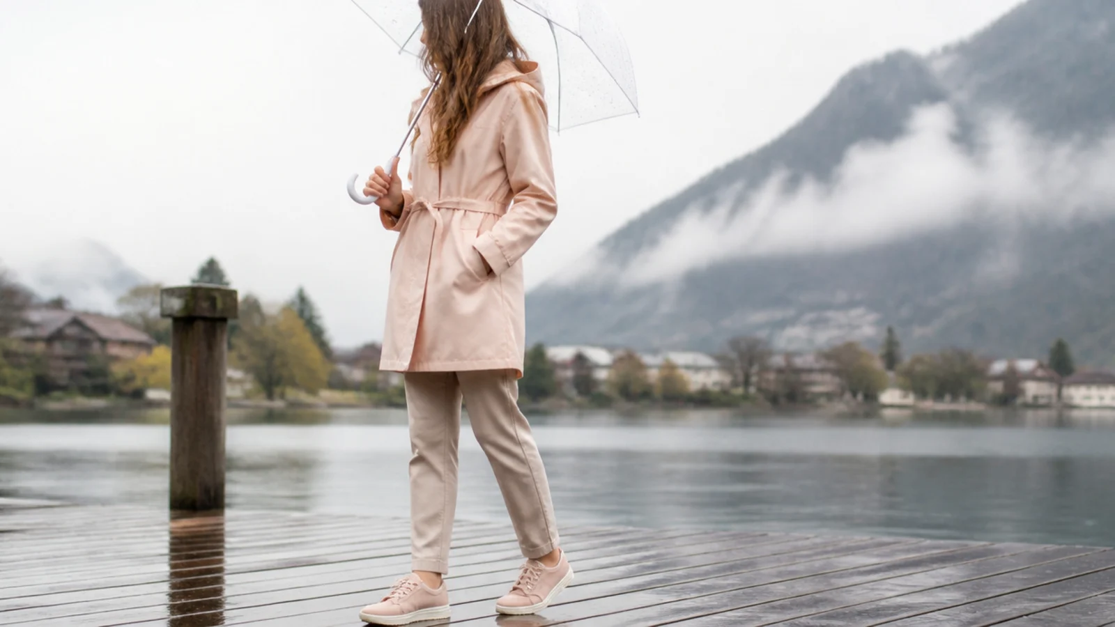 Faceless rainy vacation outfit with a belted raincoat, quick-dry pants and waterproof sneakers under a clear umbrella